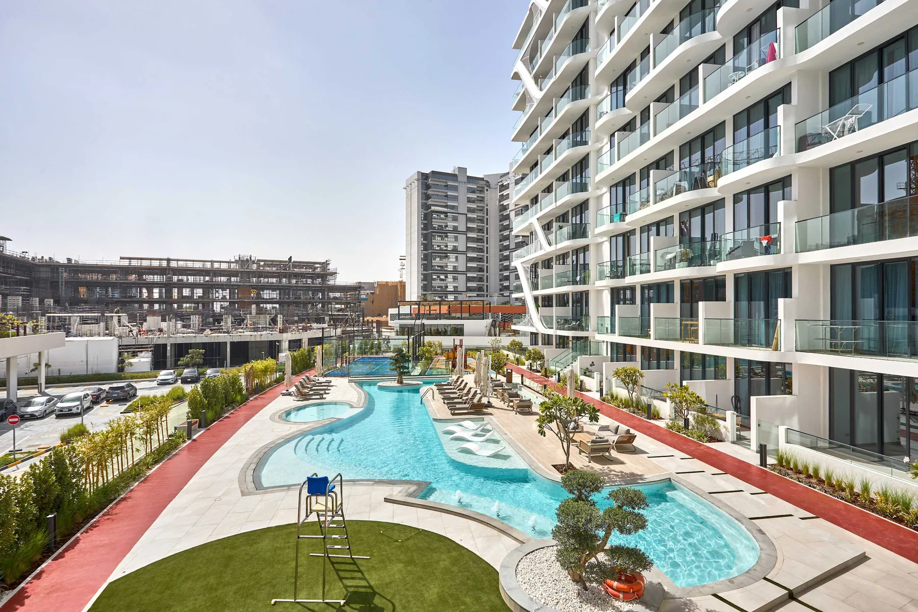 An outdoor swimming pool winds beside a modern apartment building.