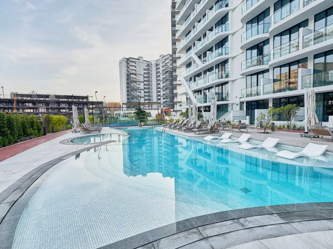 A swimming pool beside a modern building, with lounge seating along the water.