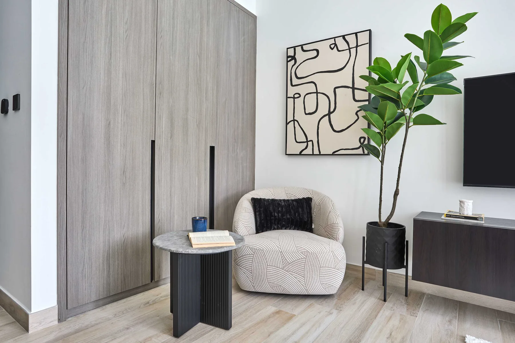 A modern living area with a rounded upholstered chair, small table, and potted plant.