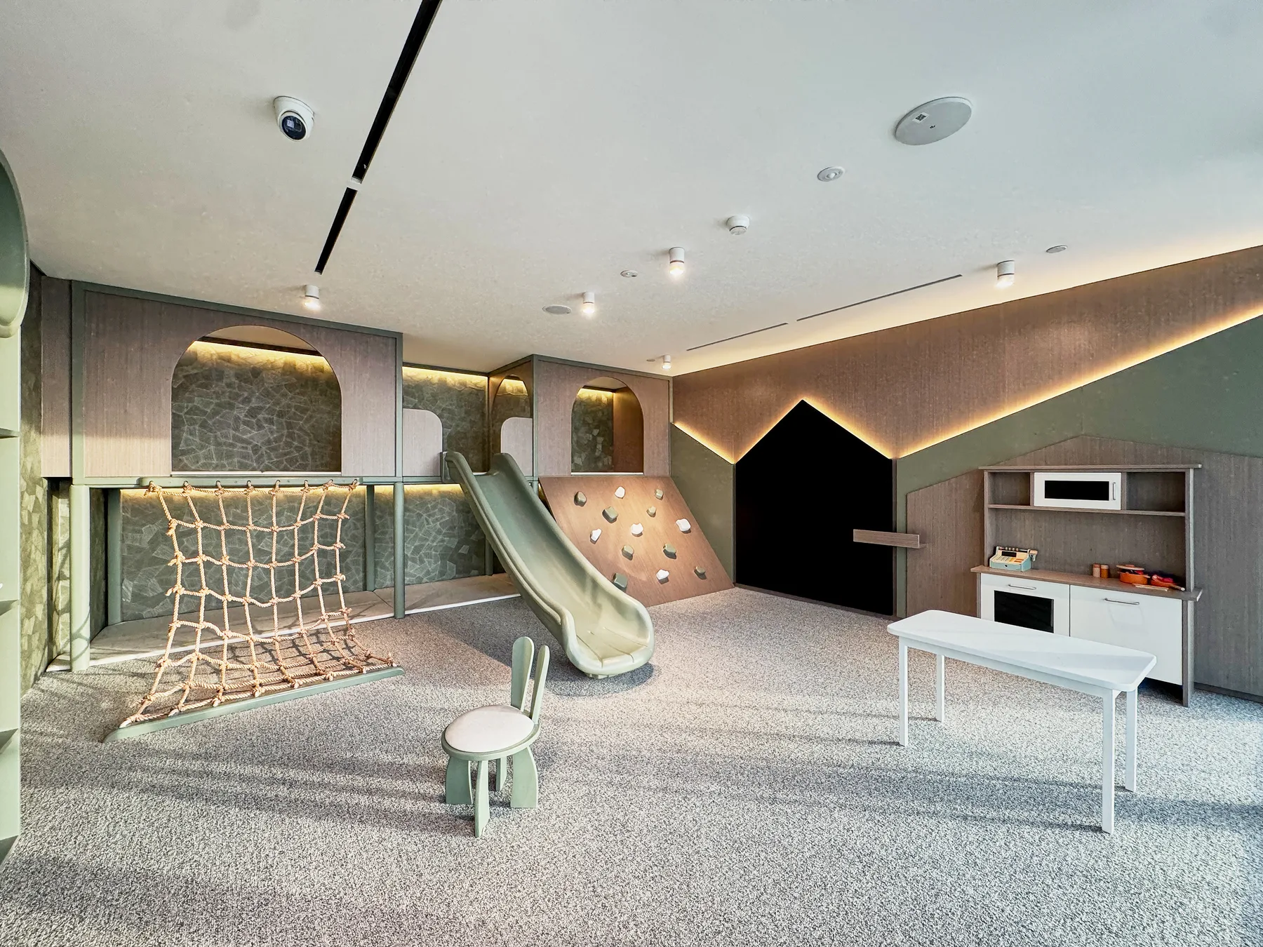 A spacious indoor playroom features a slide, climbing wall, and netted play area.