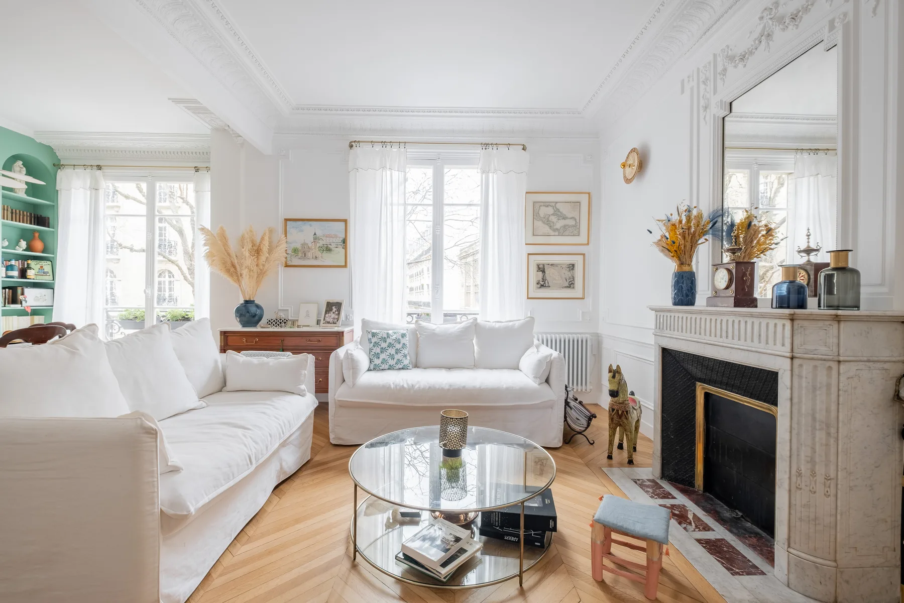 A bright living room with white seating, a glass coffee table, and a fireplace.