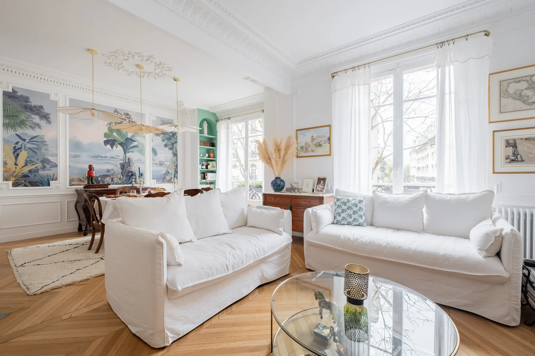 A bright living room with white seating, tall windows, and framed artwork.