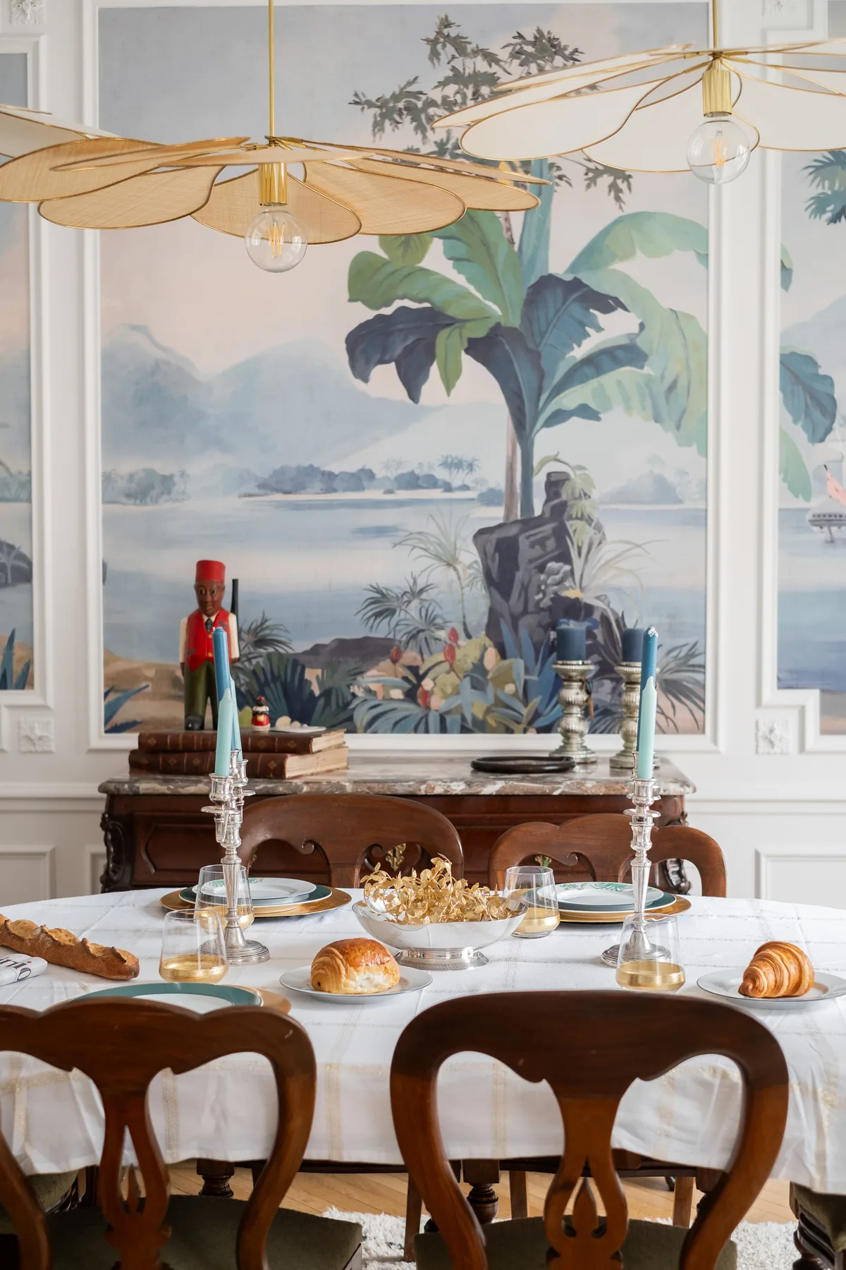 A dining room with a set table beneath pendant lights and a painted mural.