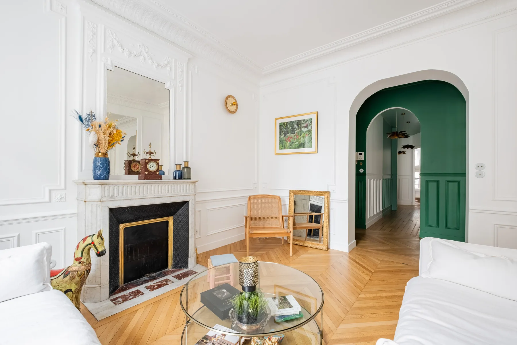A bright living room with a fireplace, glass coffee table, and green arched doorway.