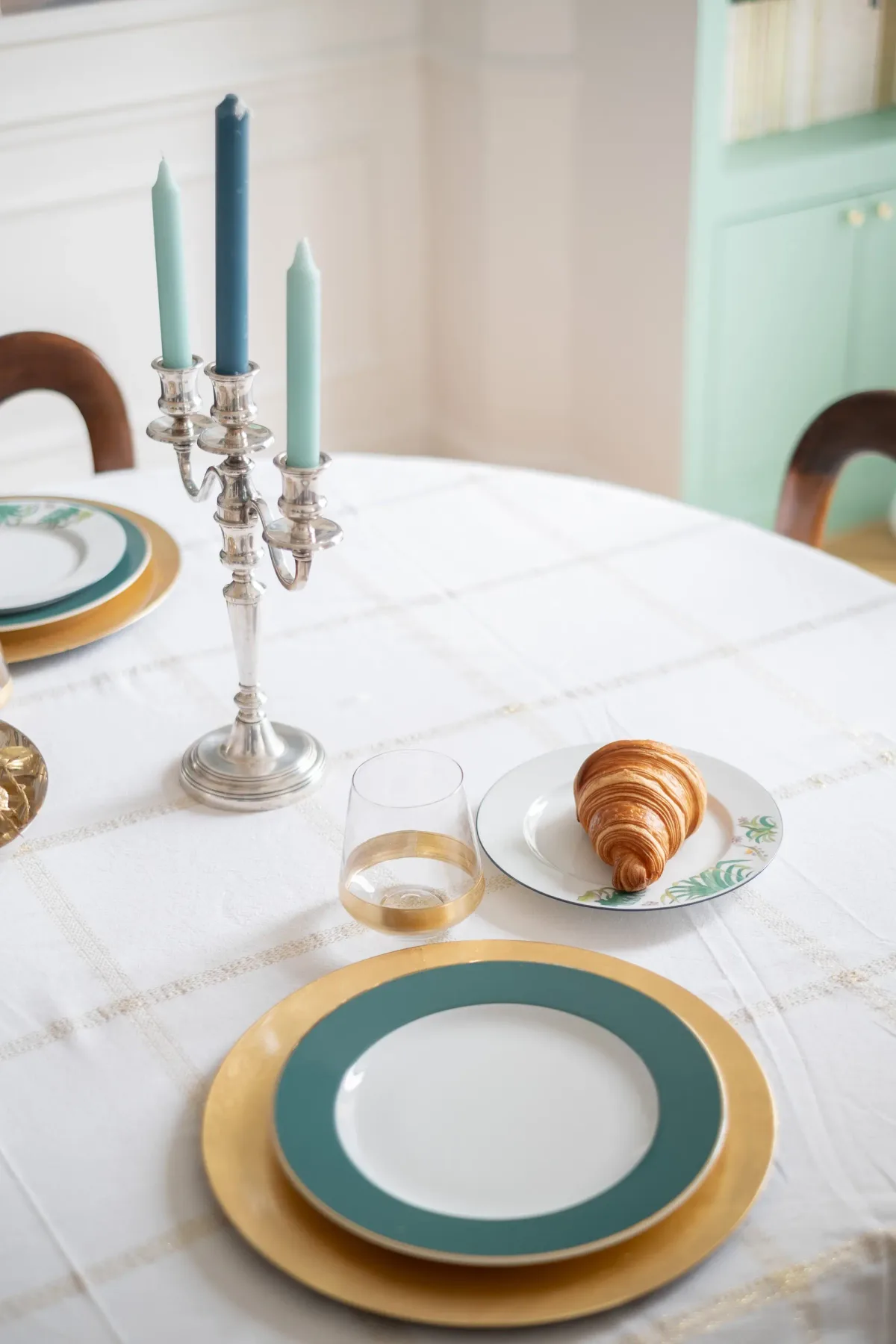 A dining table is set with plates, a croissant, and candle holders.