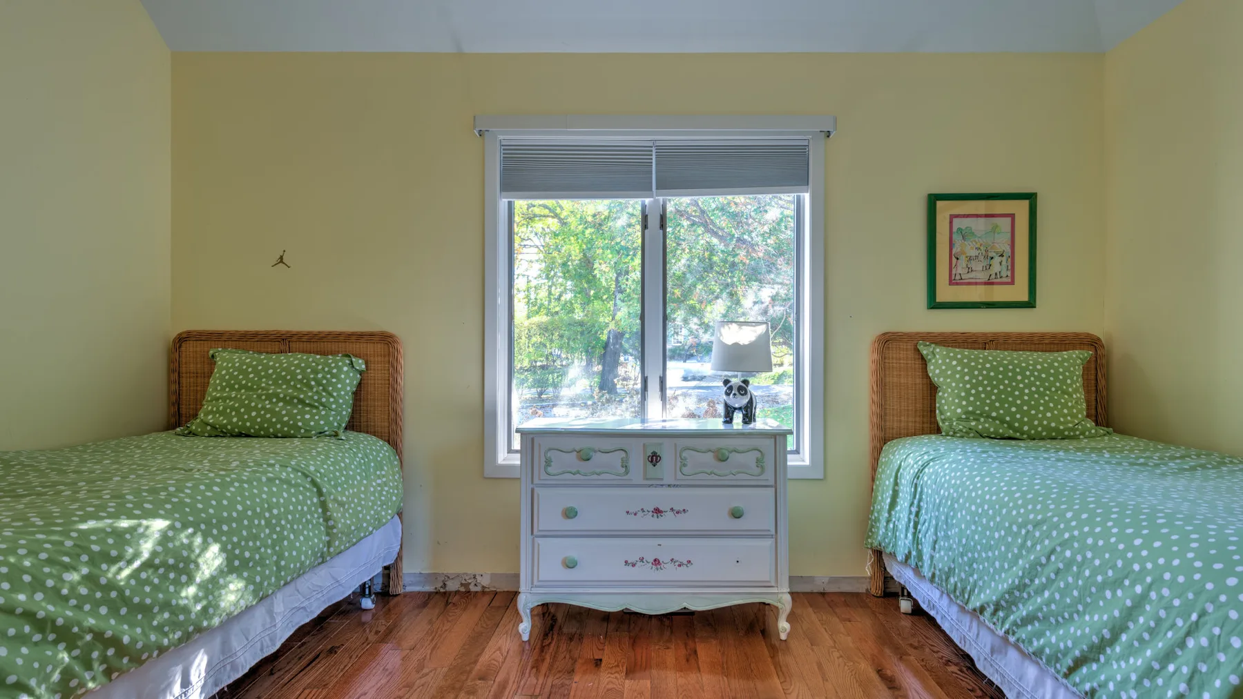 A bedroom with two green beds and a dresser beneath the window.