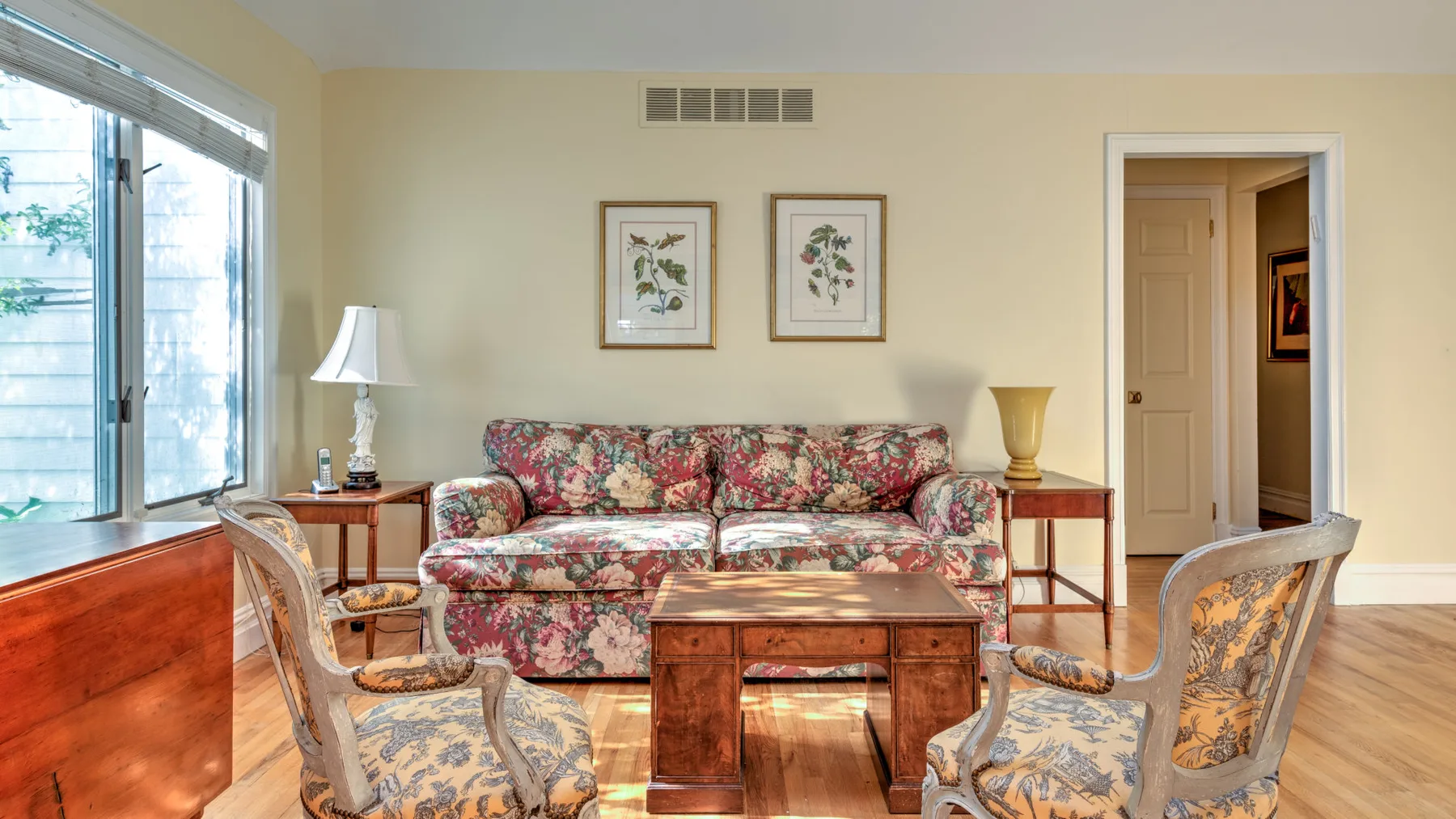 A living room with floral seating, a wooden coffee table, and framed artwork.