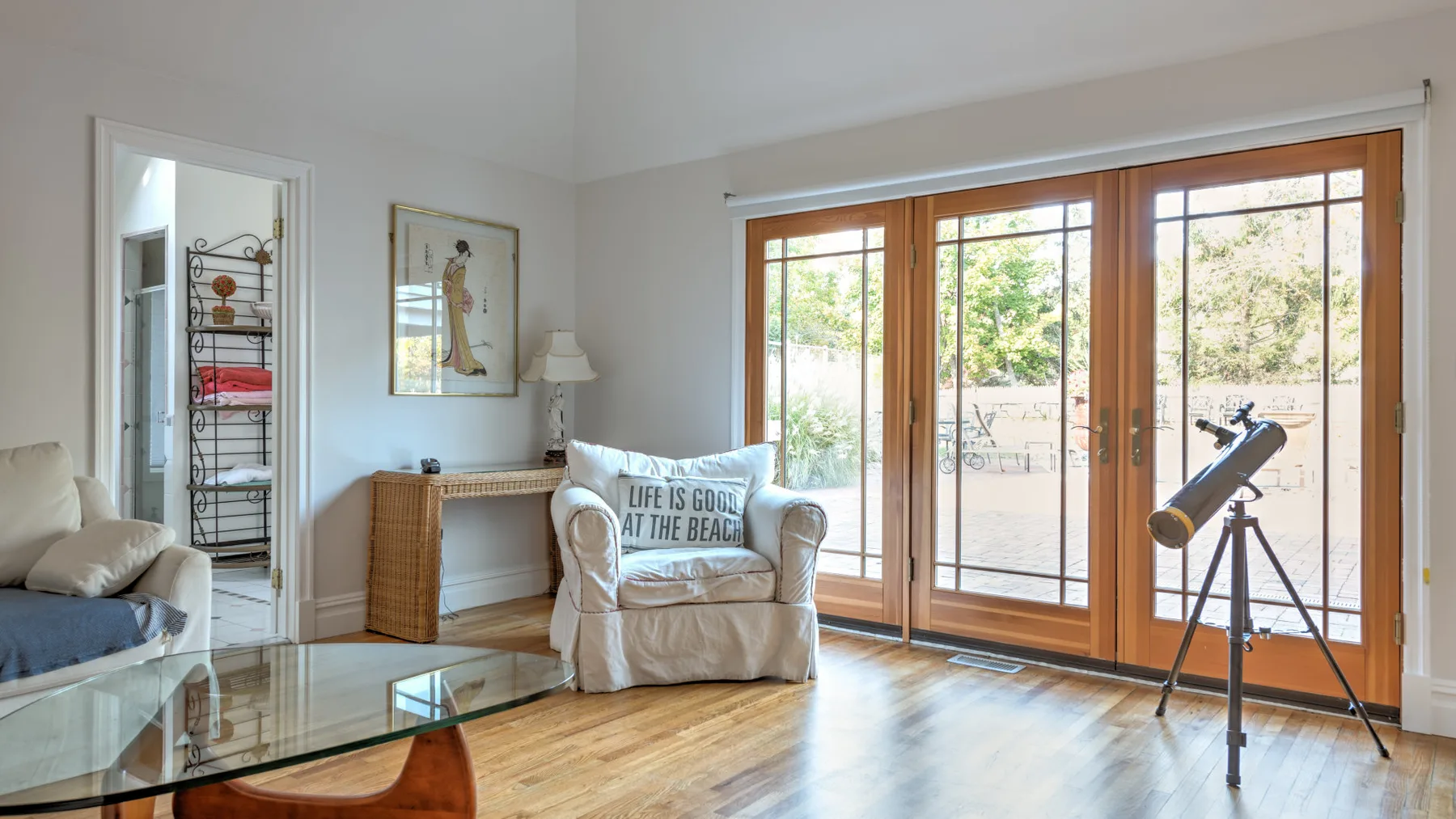 A bright living room with seating, a glass coffee table, and large windows.