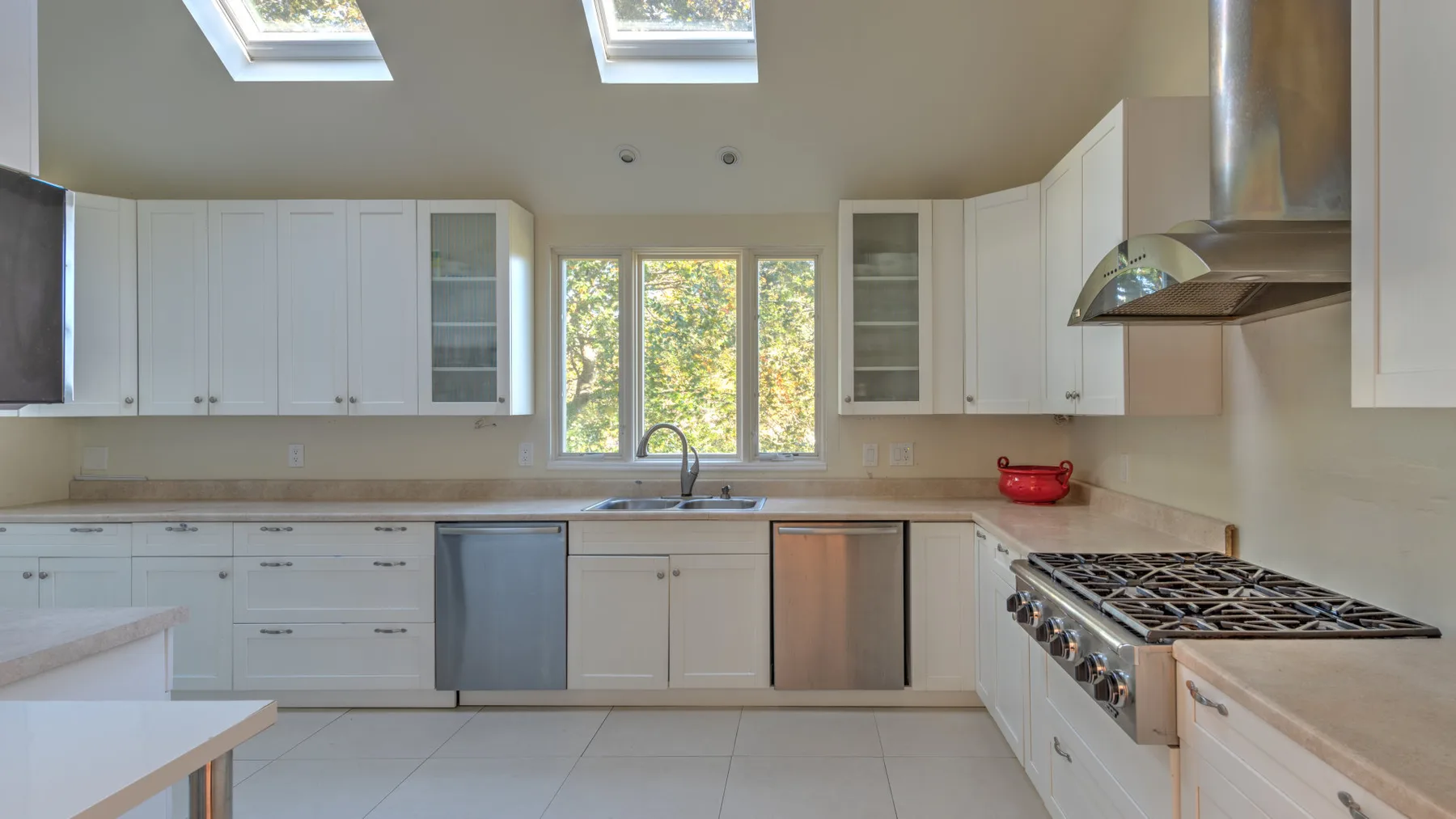 A bright kitchen with white cabinets, a central window, and a long countertop.