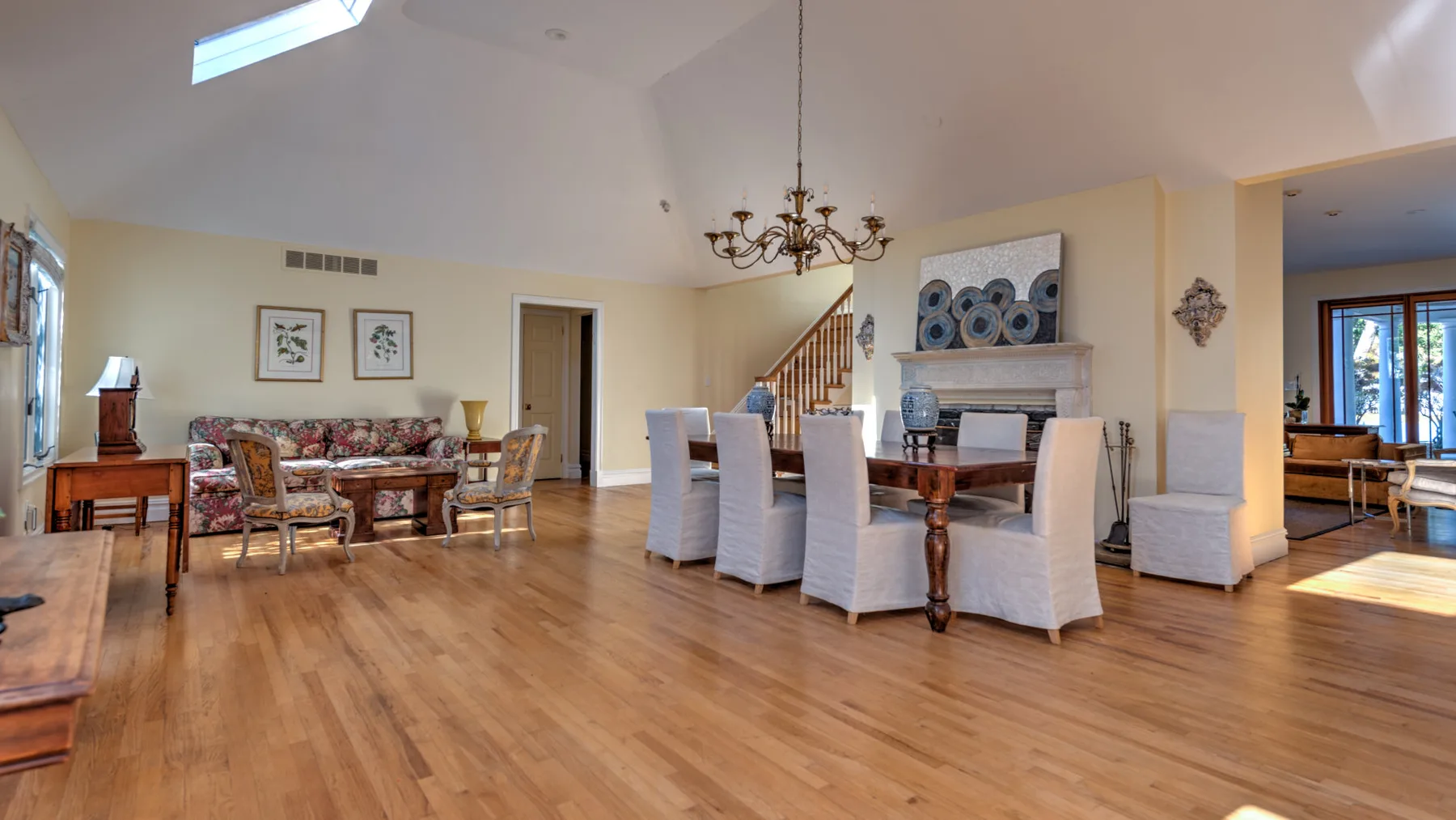 A spacious dining and living area with a long table, seating, and a chandelier.