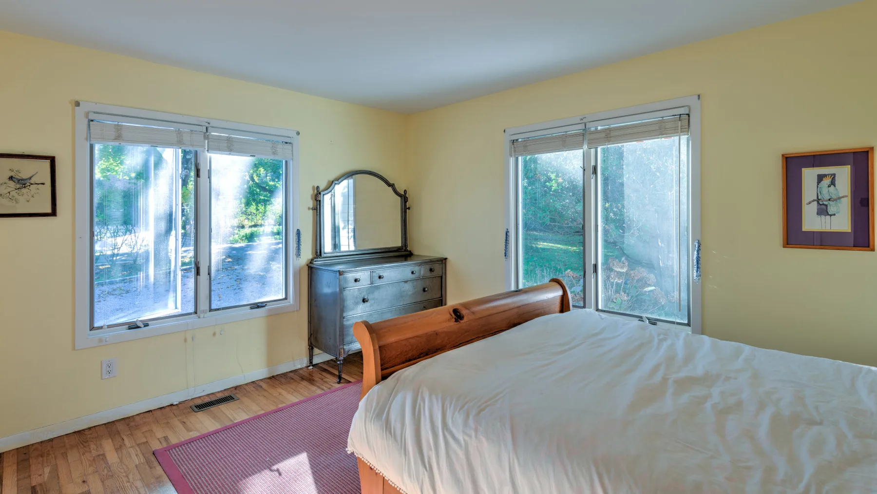 A bedroom with a bed, dresser, and windows overlooking greenery.