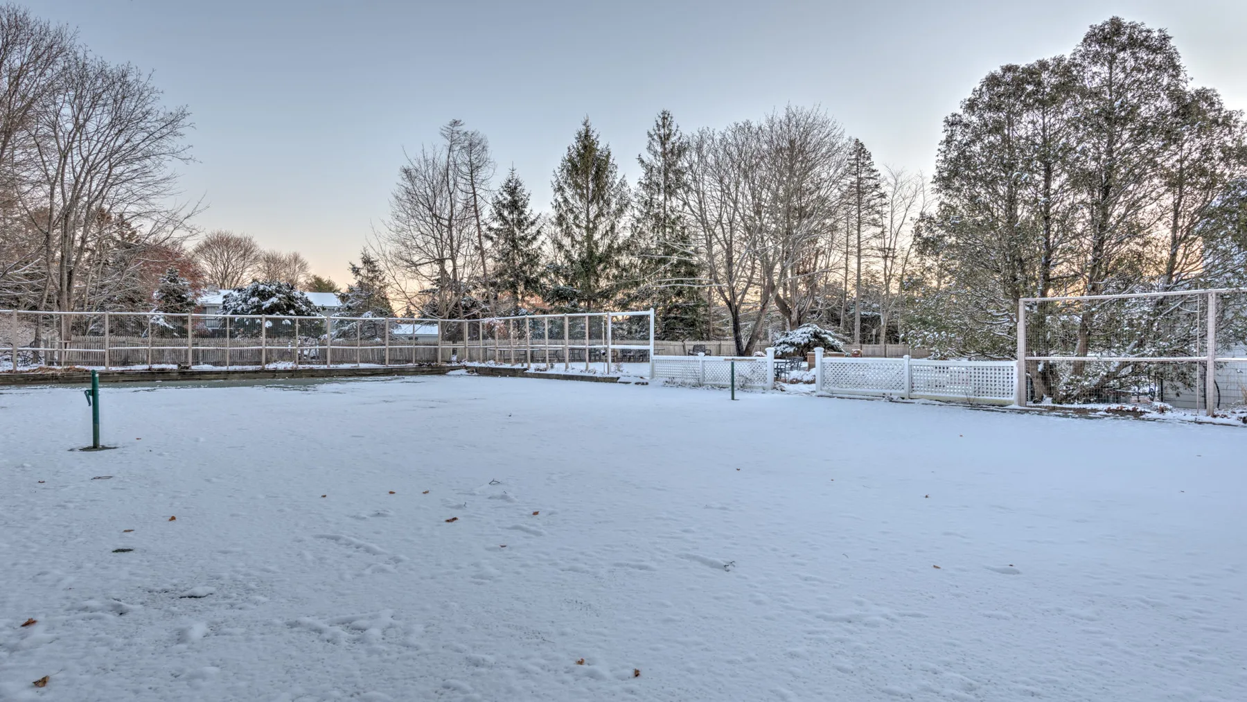A snow-covered outdoor yard is enclosed by fencing and leafless trees.