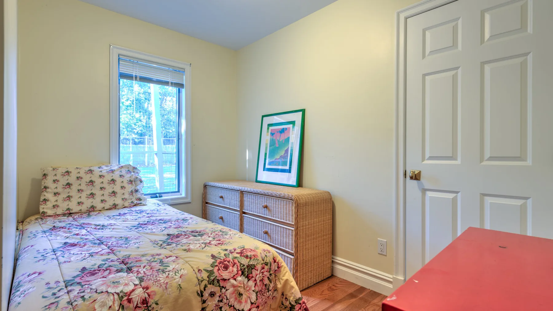 A bedroom with a floral bedspread and a wicker-front dresser.