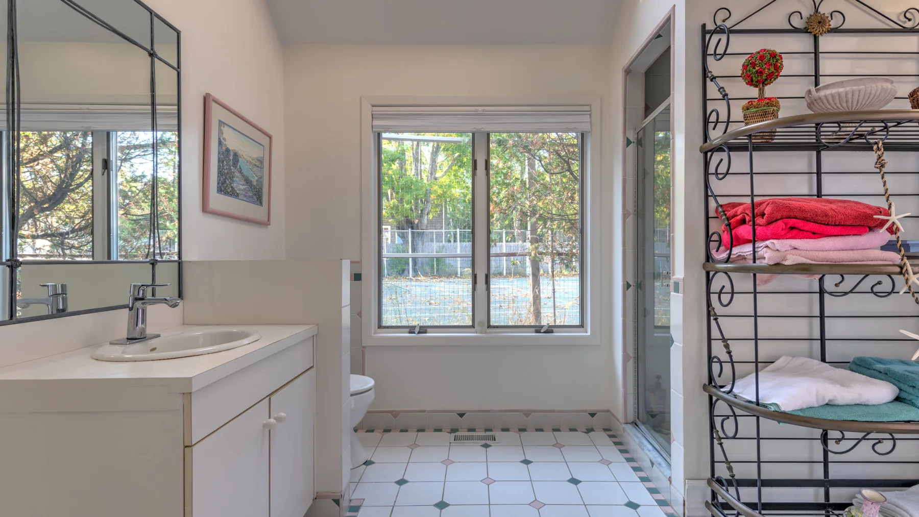 A bright bathroom with a sink, wall mirror, and window overlooking greenery.