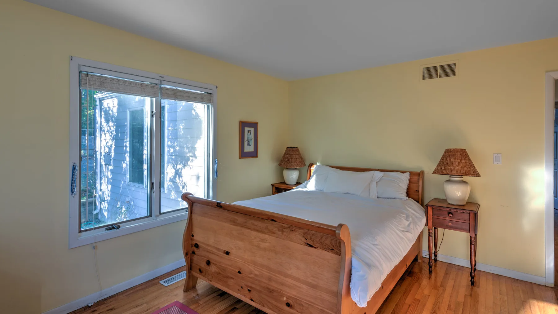 A bedroom with a wooden bed, white bedding, and a large window.