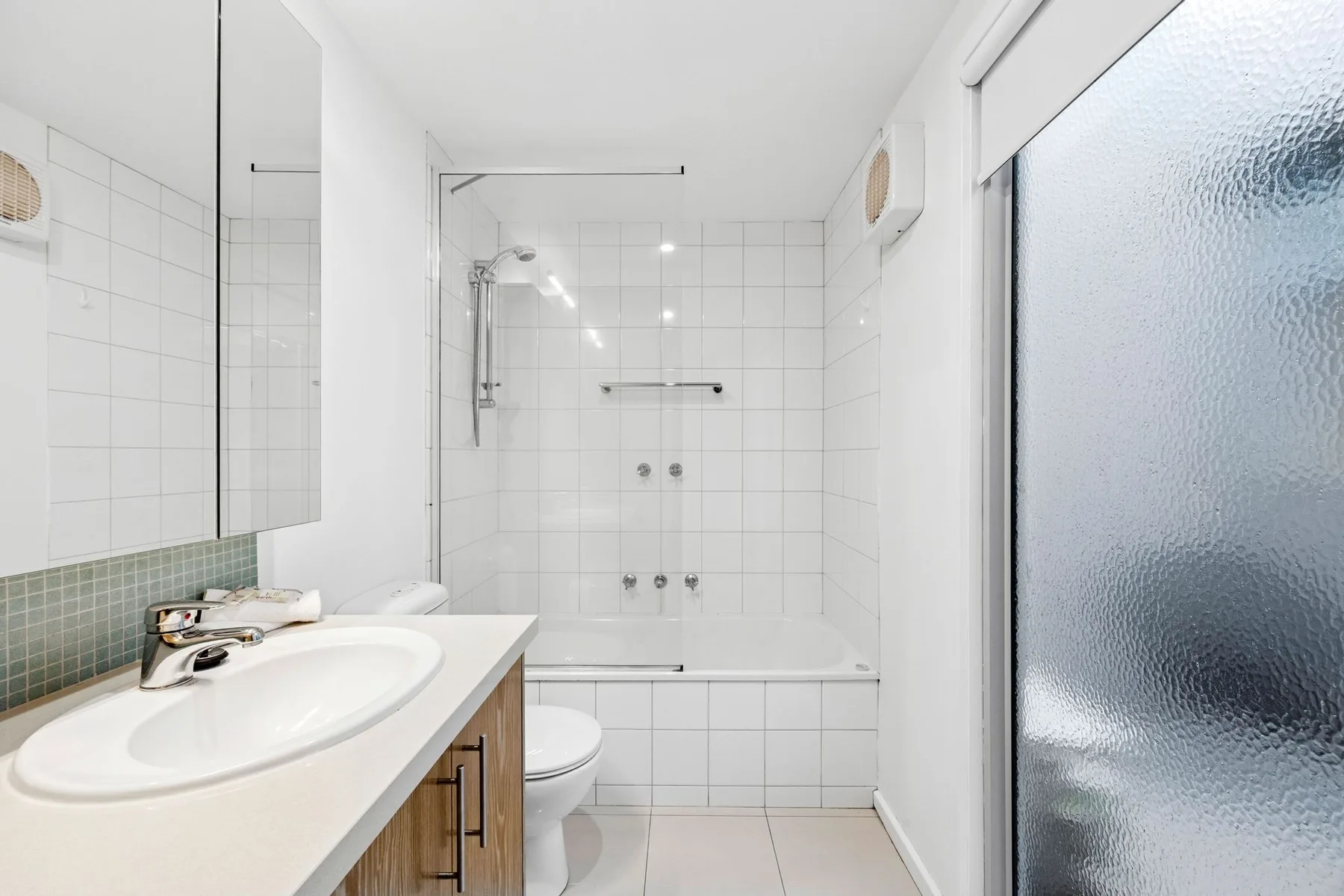 Un baño con azulejos, bañera, lavabo y puerta de vidrio esmerilado.