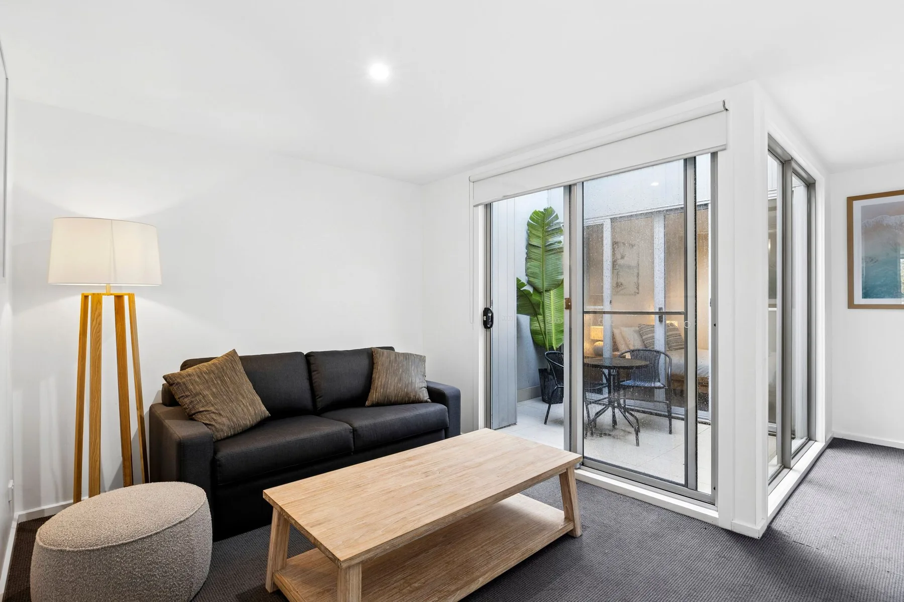 Una sala de estar con asientos oscuros y puertas corredizas de vidrio hacia un patio.