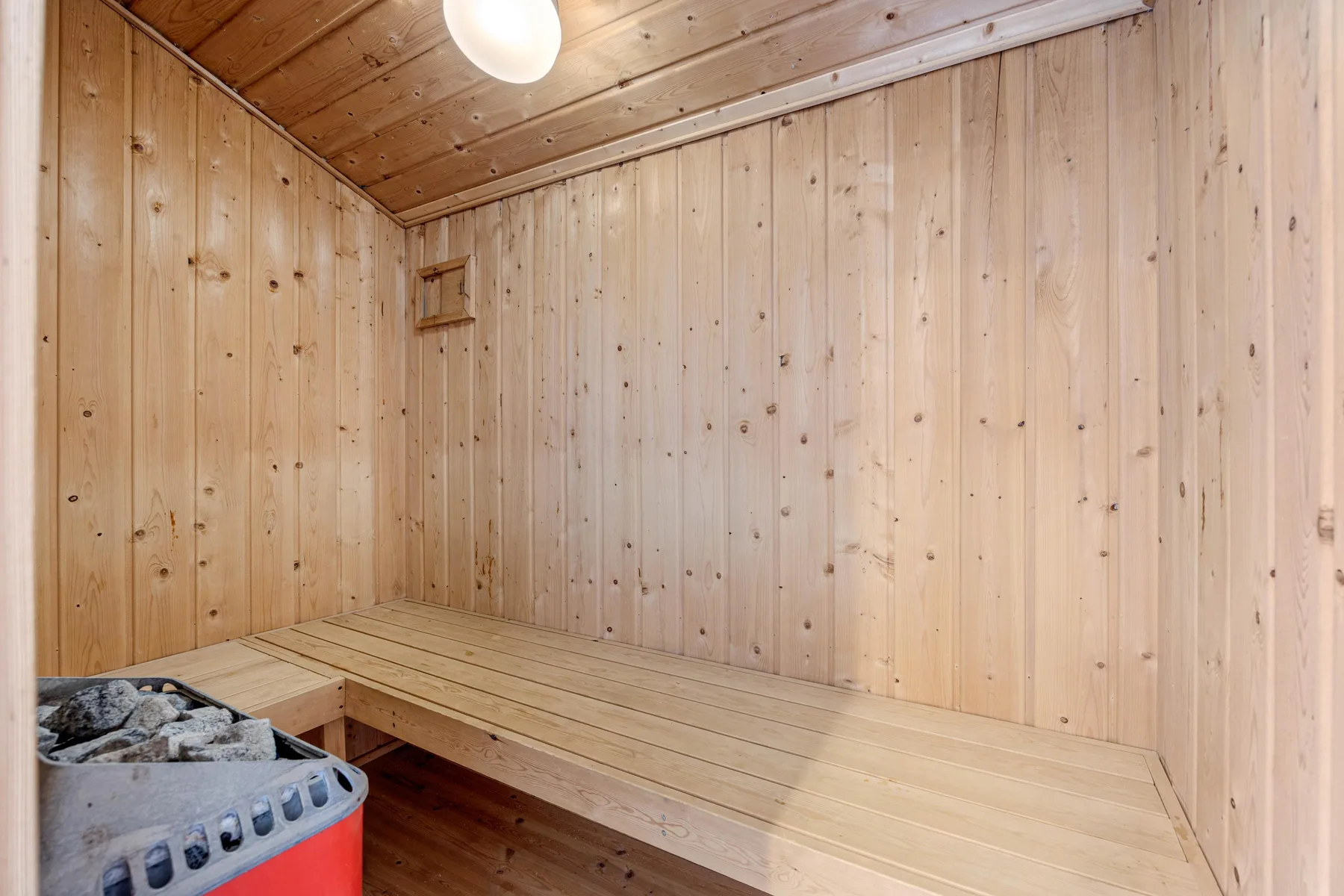 Una sauna revestida de madera con un banco y un calentador lleno de piedras.