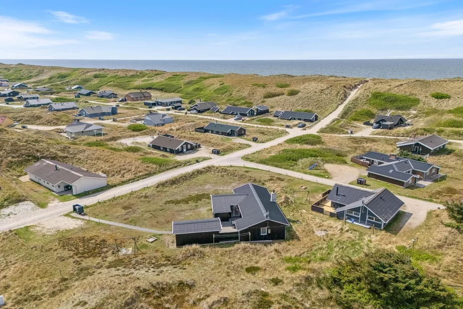 Vista aérea de casas dispersas junto a caminos de arena entre dunas costeras.