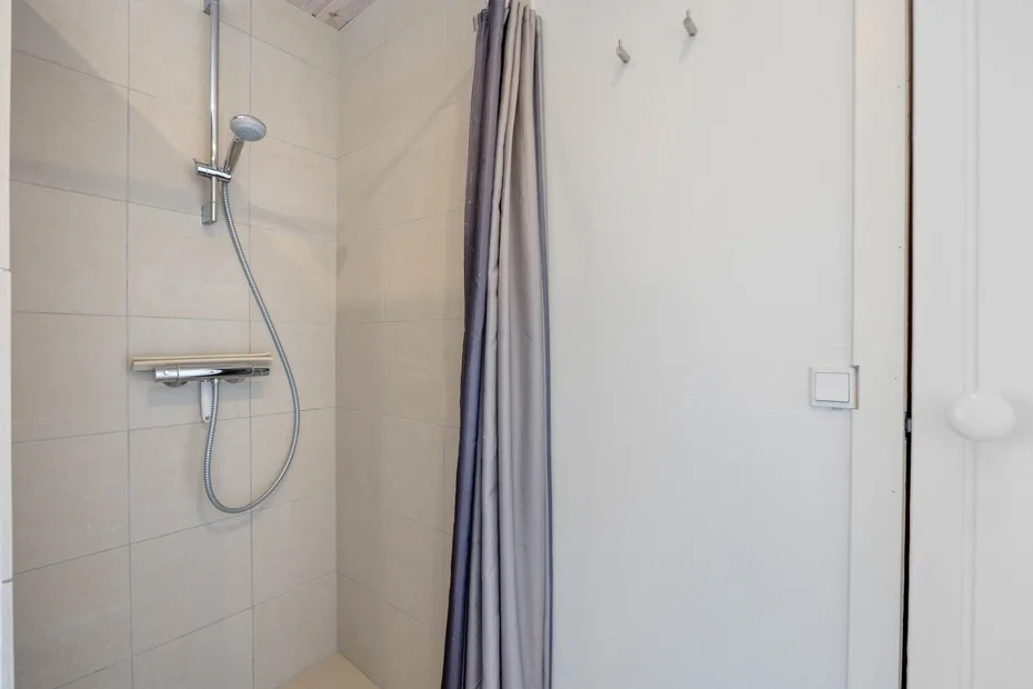 Zona de ducha con azulejos, ducha de mano y cortina.