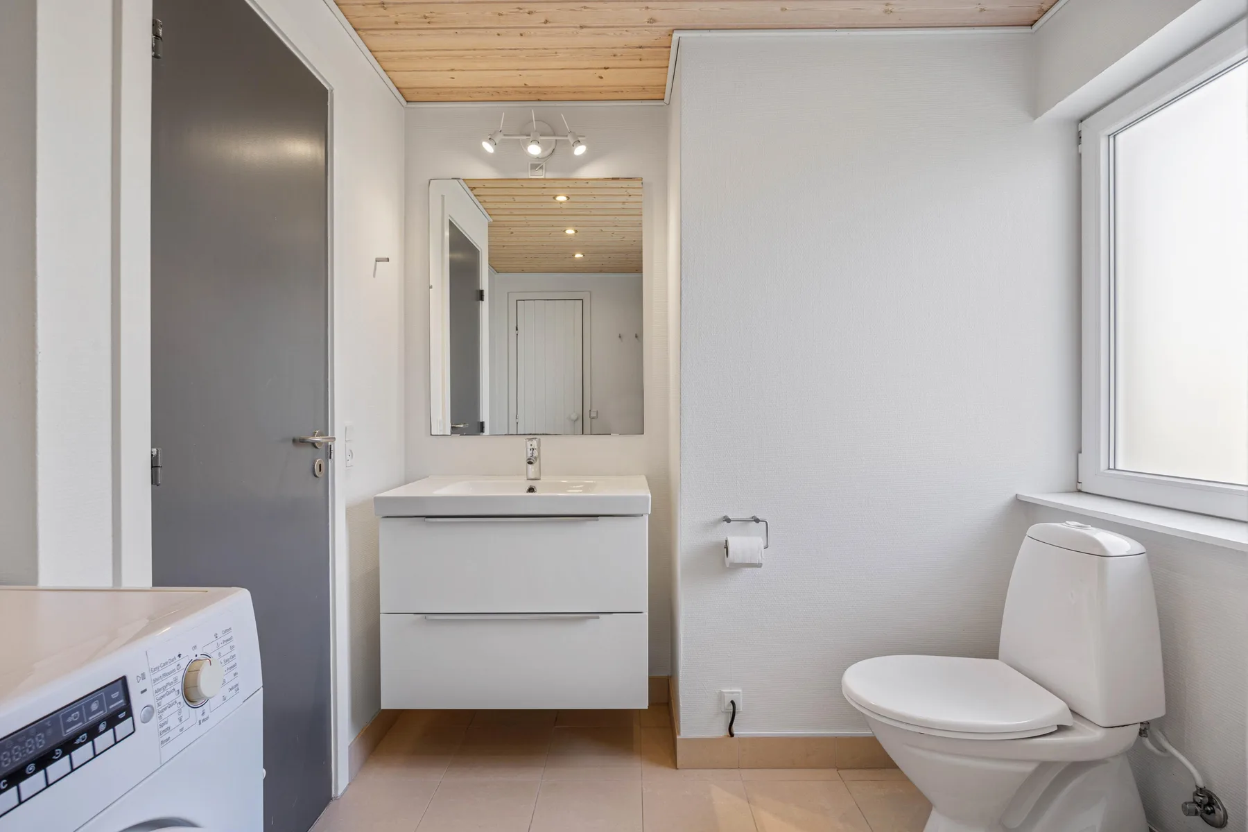 Un baño luminoso con lavabo, espejo, inodoro y lavadora.