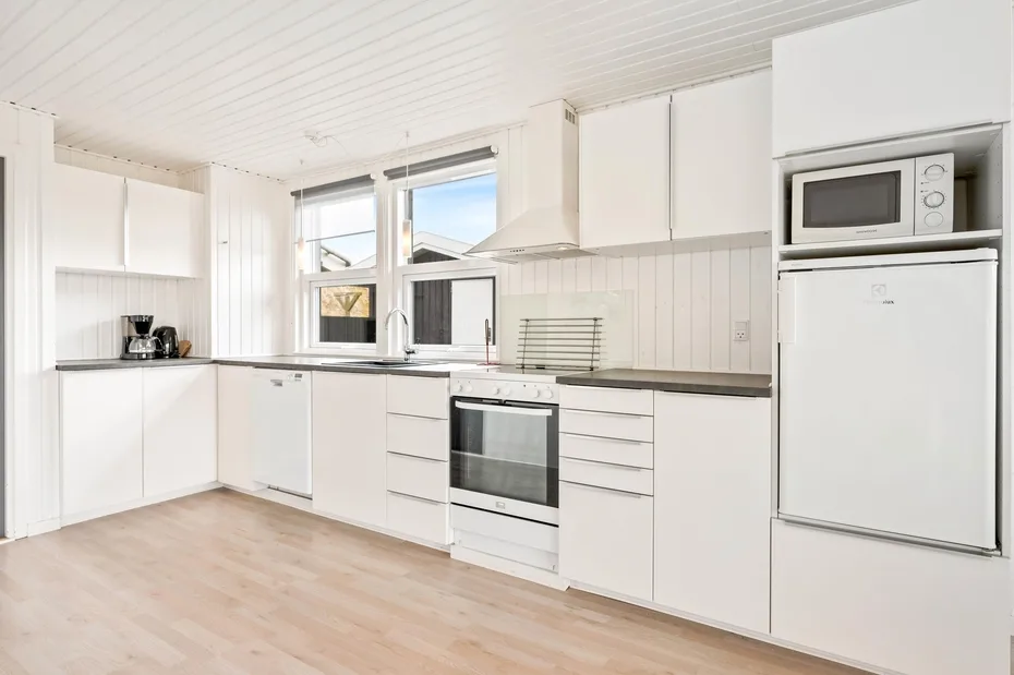 Una cocina blanca y luminosa con estufa, encimera y electrodomésticos integrados.