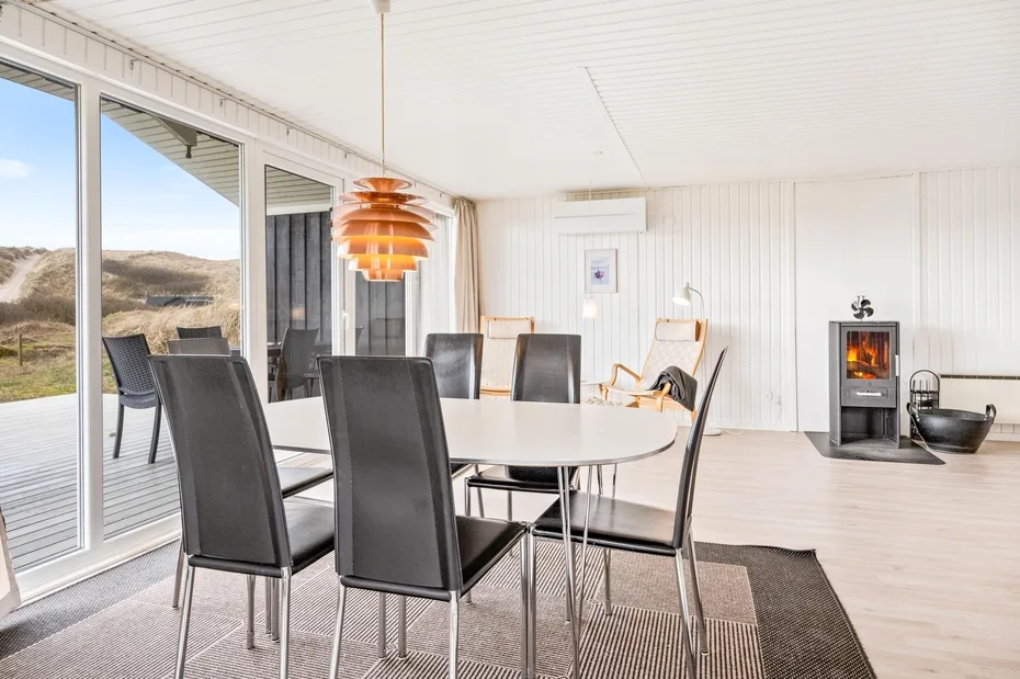 Un comedor luminoso con una mesa y asientos oscuros junto a grandes ventanales.