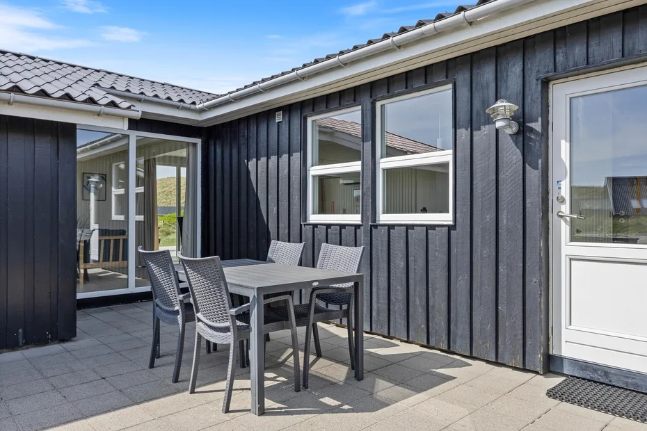 Un patio exterior con mesa de comedor y asientos junto a un edificio de revestimiento oscuro.