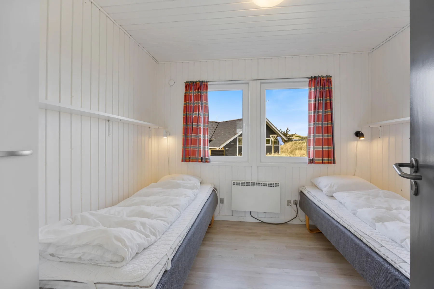 Un dormitorio luminoso con dos camas individuales y una ventana con cortinas a cuadros.