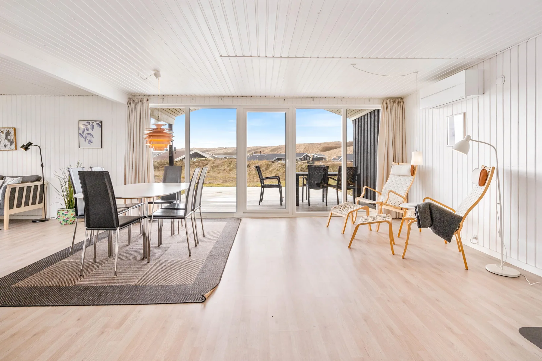 Una luminosa zona de comedor y estar se abre a grandes ventanas con vistas a un paisaje costero.