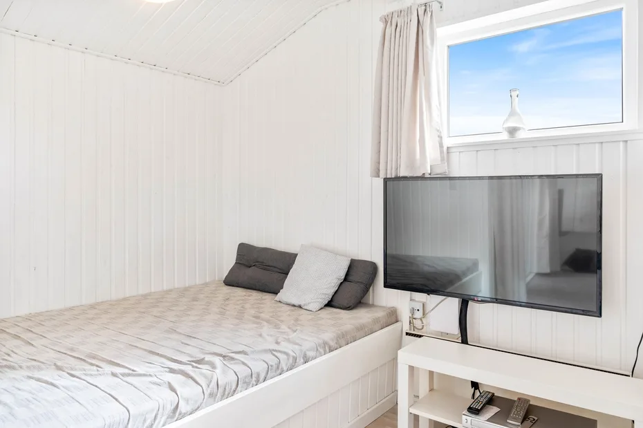 Un dormitorio luminoso con una cama junto a un televisor y una ventana.