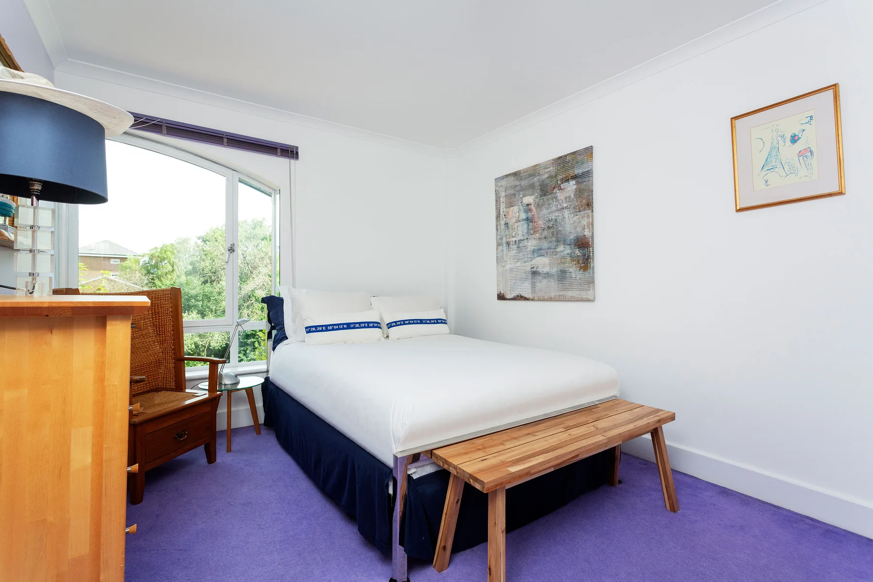 A bedroom with a bed, wooden bench, and purple carpet.