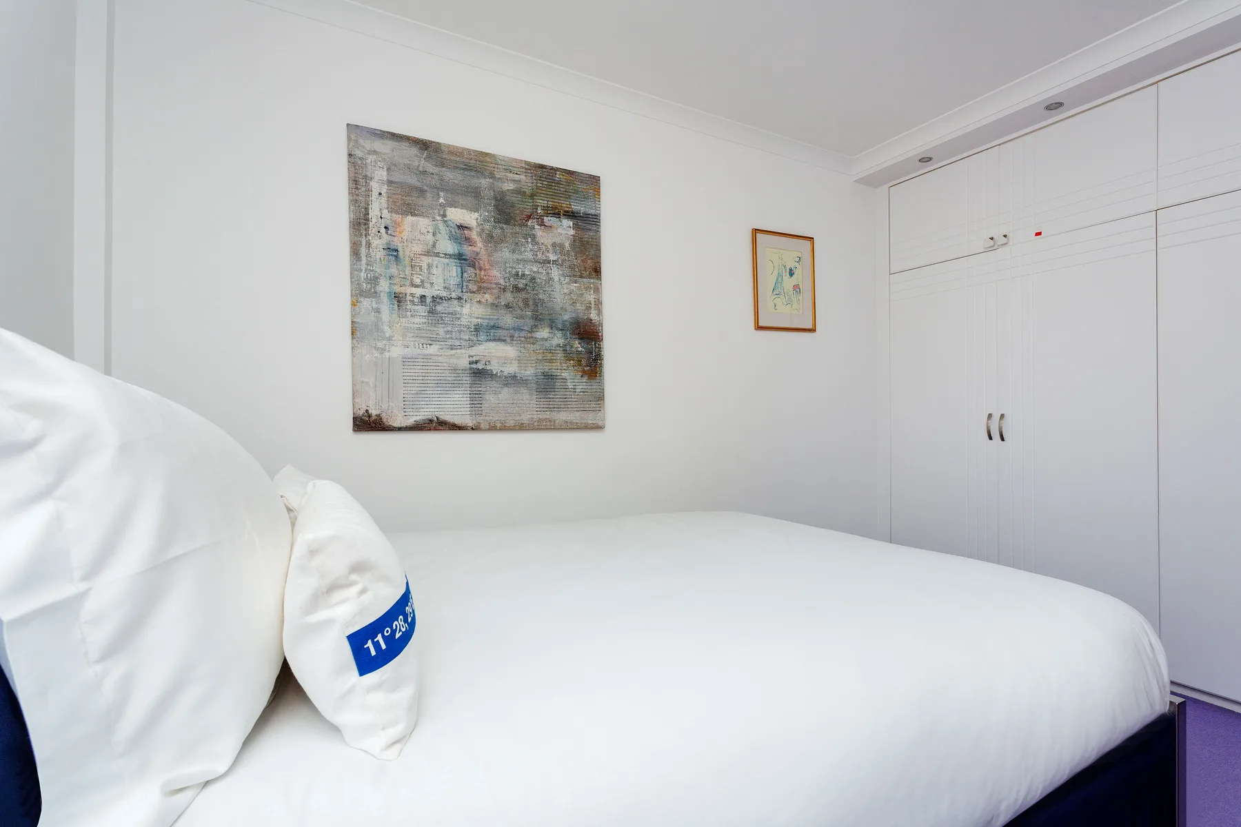 Un dormitorio con una cama bien tendida y cuadros en la pared.