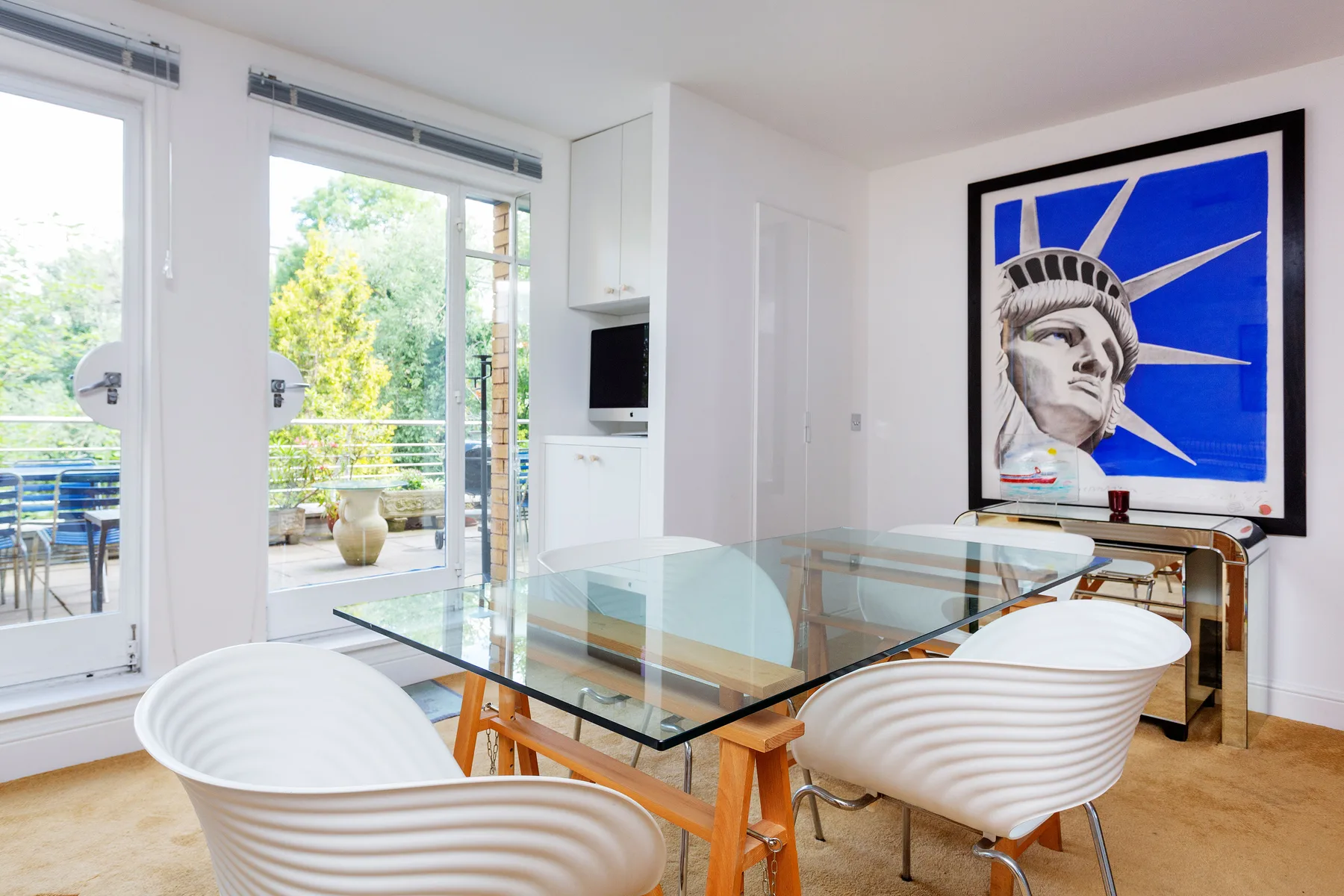 A dining area with a glass table and white seating beside large windows.