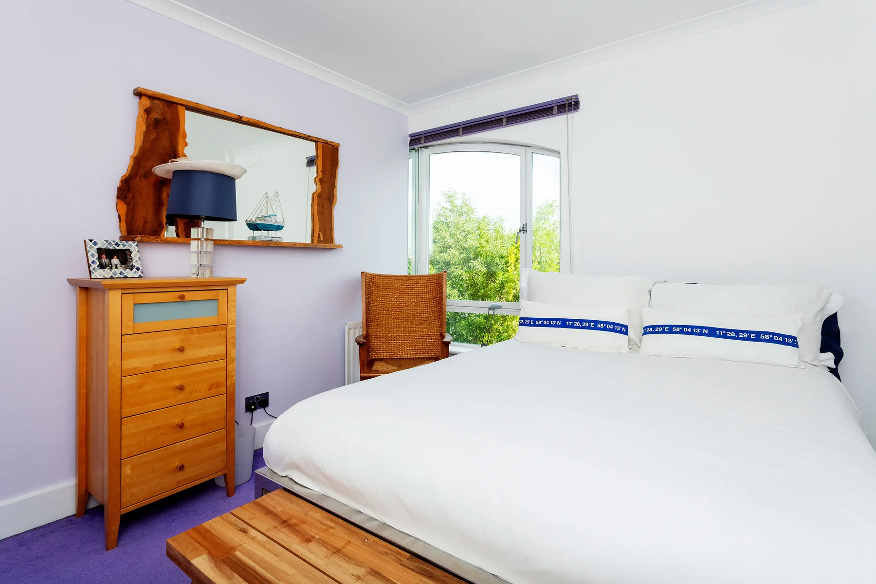 Un dormitorio luminoso con ropa de cama blanca y una ventana grande con vistas a la vegetación.