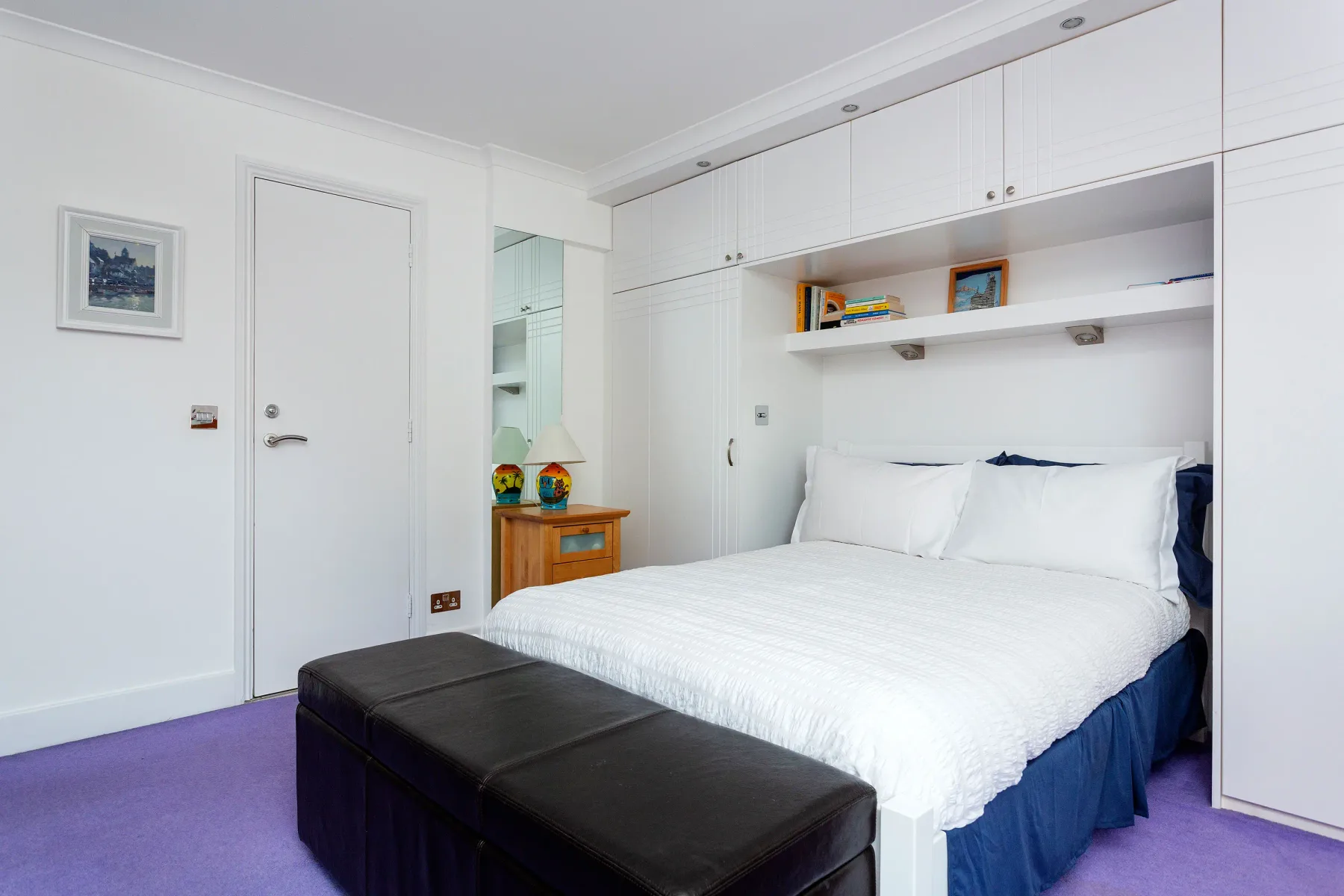 Un dormitorio con una cama blanca y un banco negro a sus pies.