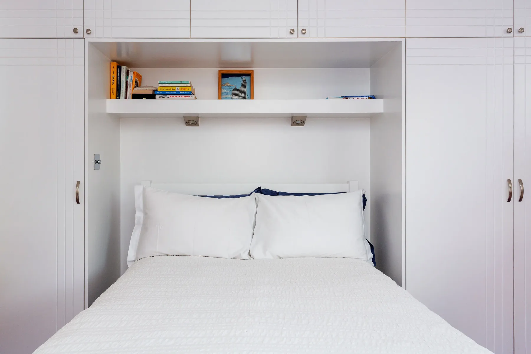 Una cama con ropa de cama blanca está integrada en una pared de armarios.
