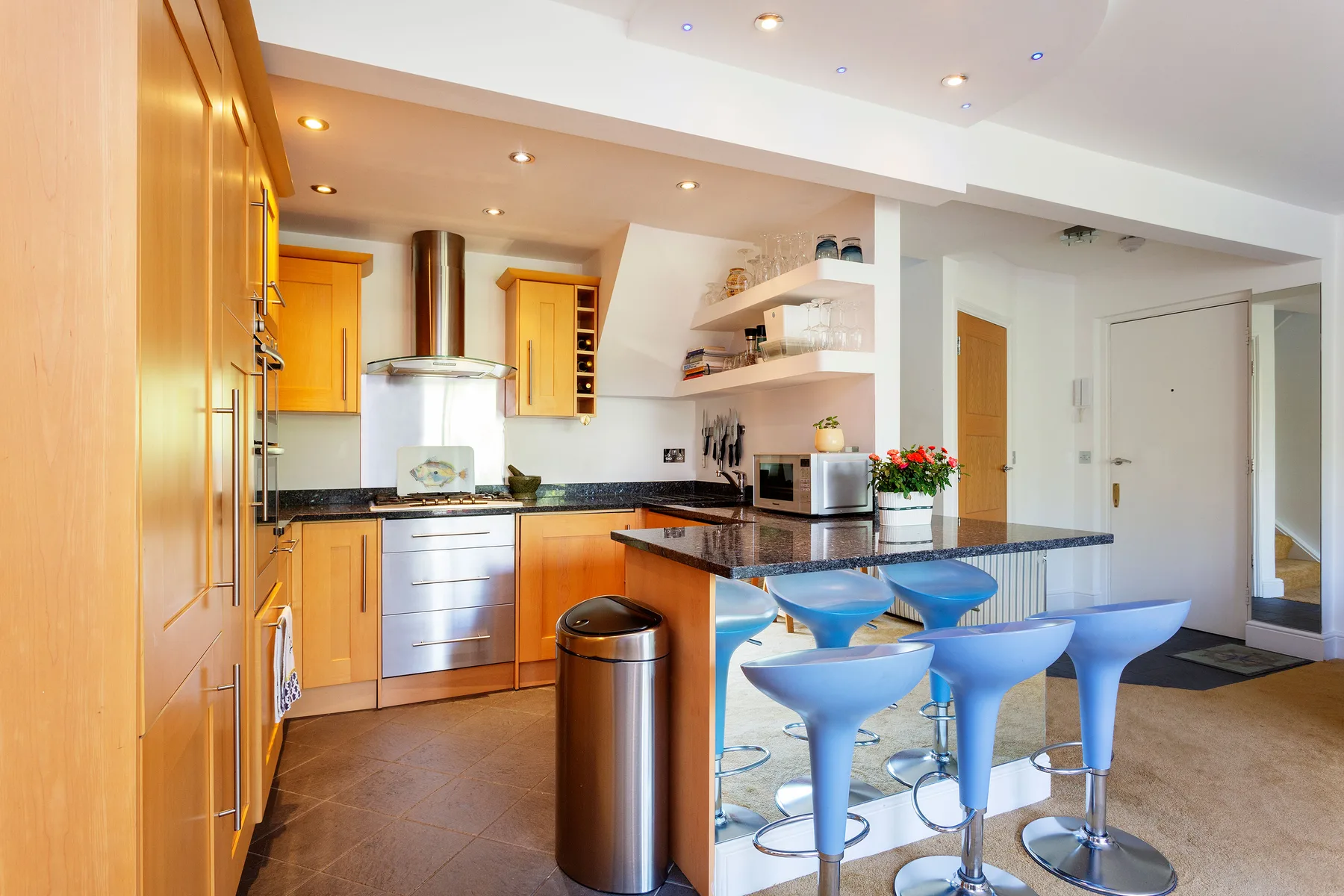 A bright kitchen with wooden cabinets, a central island, and blue bar stools.