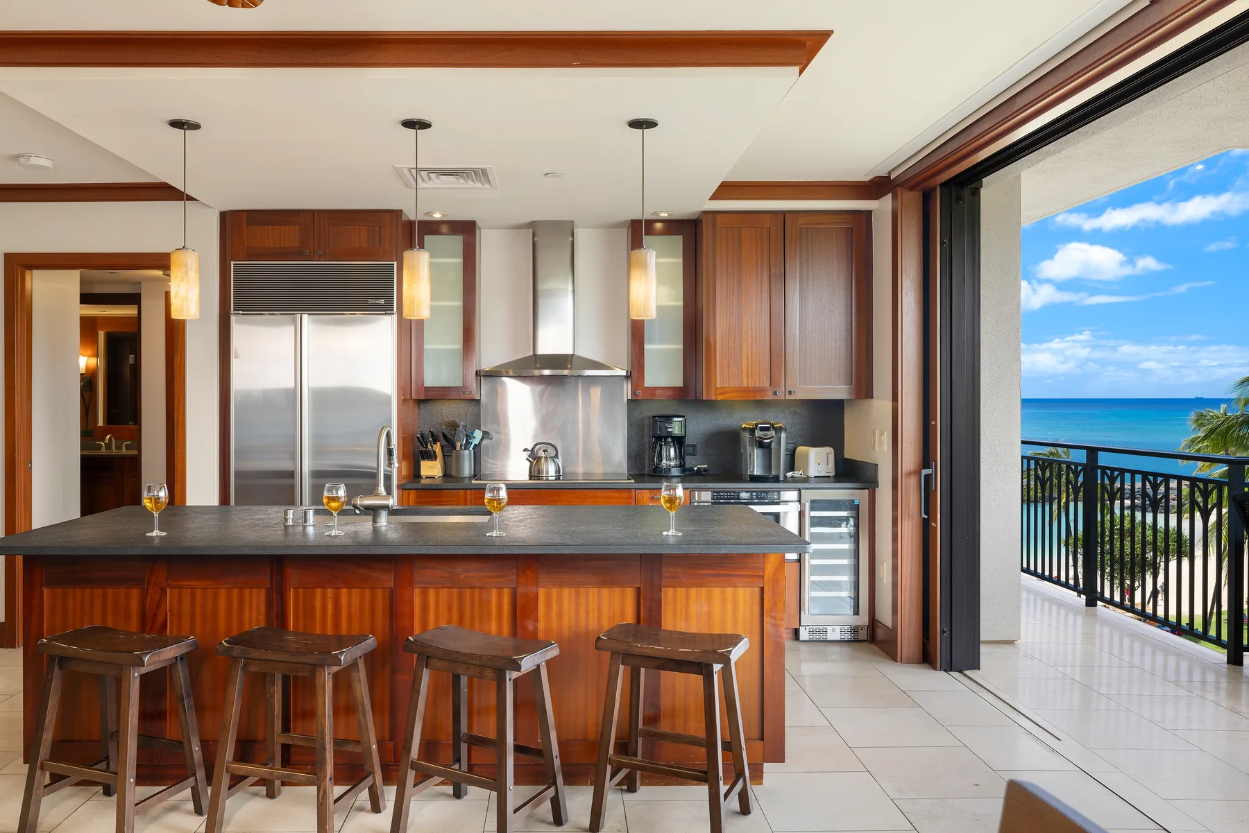 Una cocina con barra y taburetes se abre a un balcón con vistas al mar.