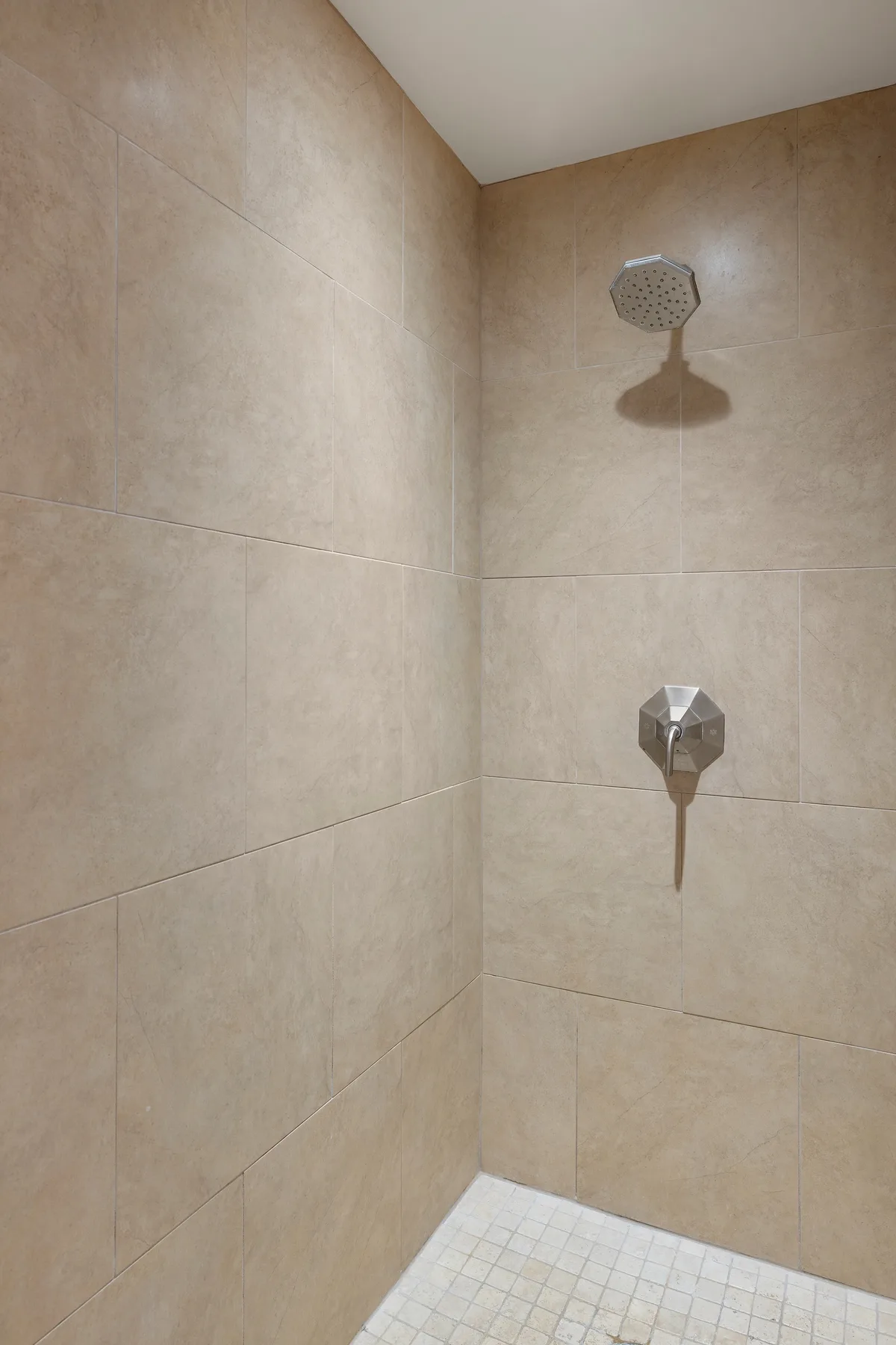 Una ducha con azulejos, cabezal de ducha y control en la pared.