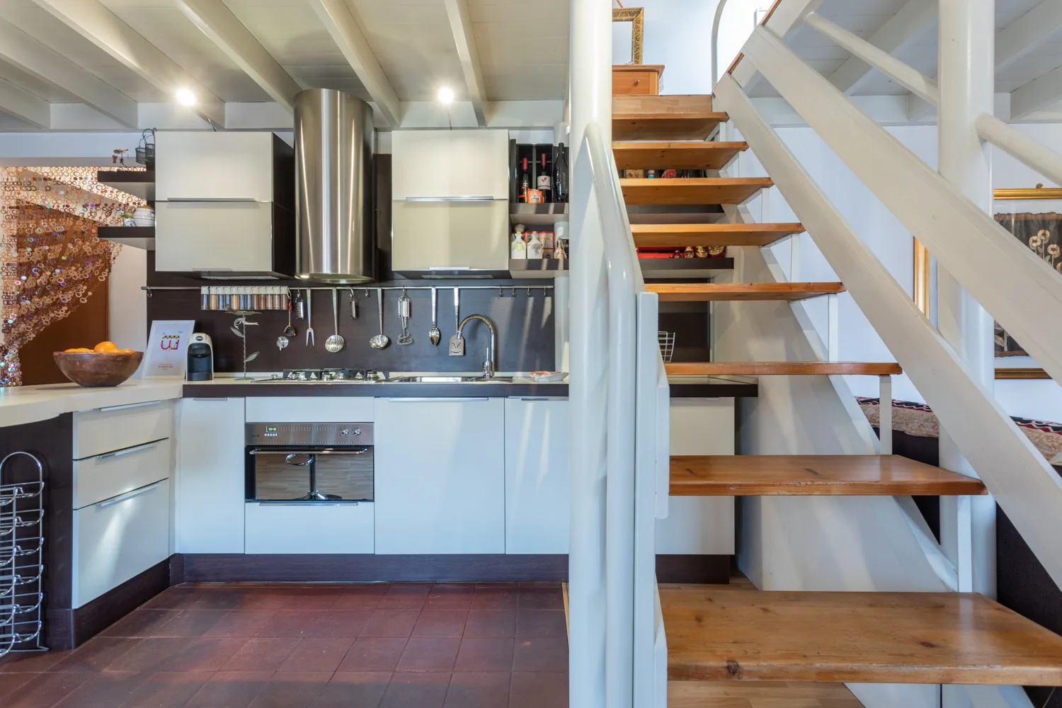 A kitchen with a stainless-steel range hood beside a wooden staircase.