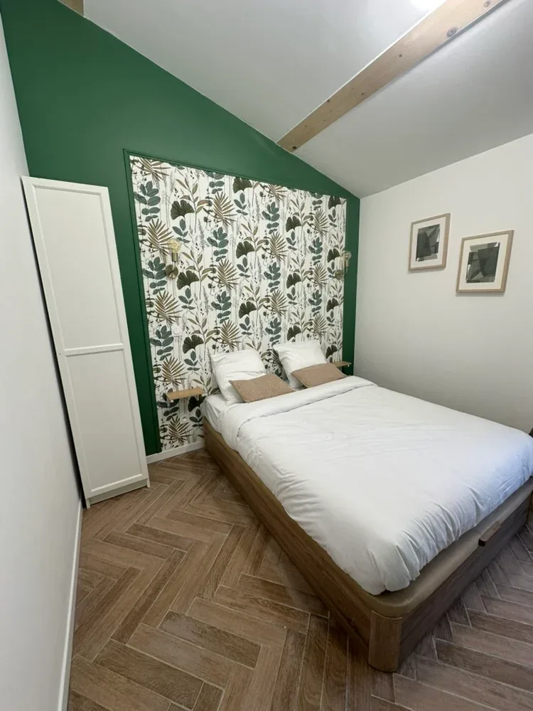 A bedroom with a bed beneath a botanical patterned wall hanging.