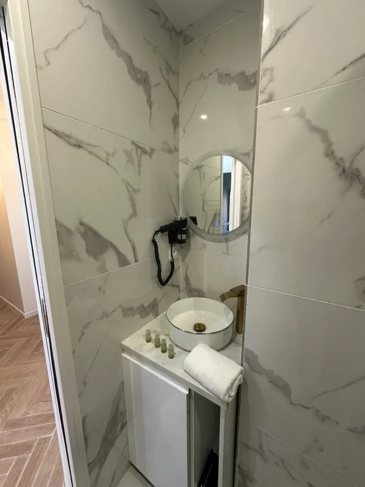 A compact bathroom vanity with a vessel sink, round mirror, and wall-mounted shower fixture.