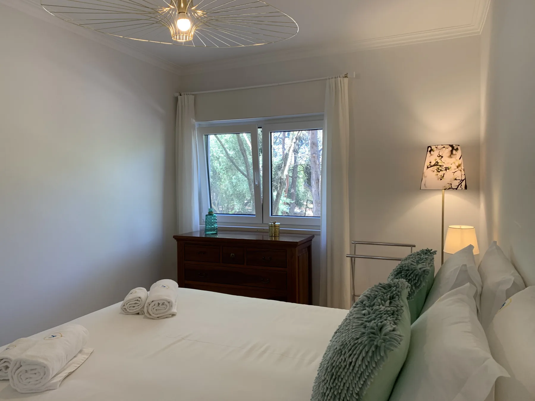 Dormitorio con cama, cómoda y una ventana con vista a los árboles.