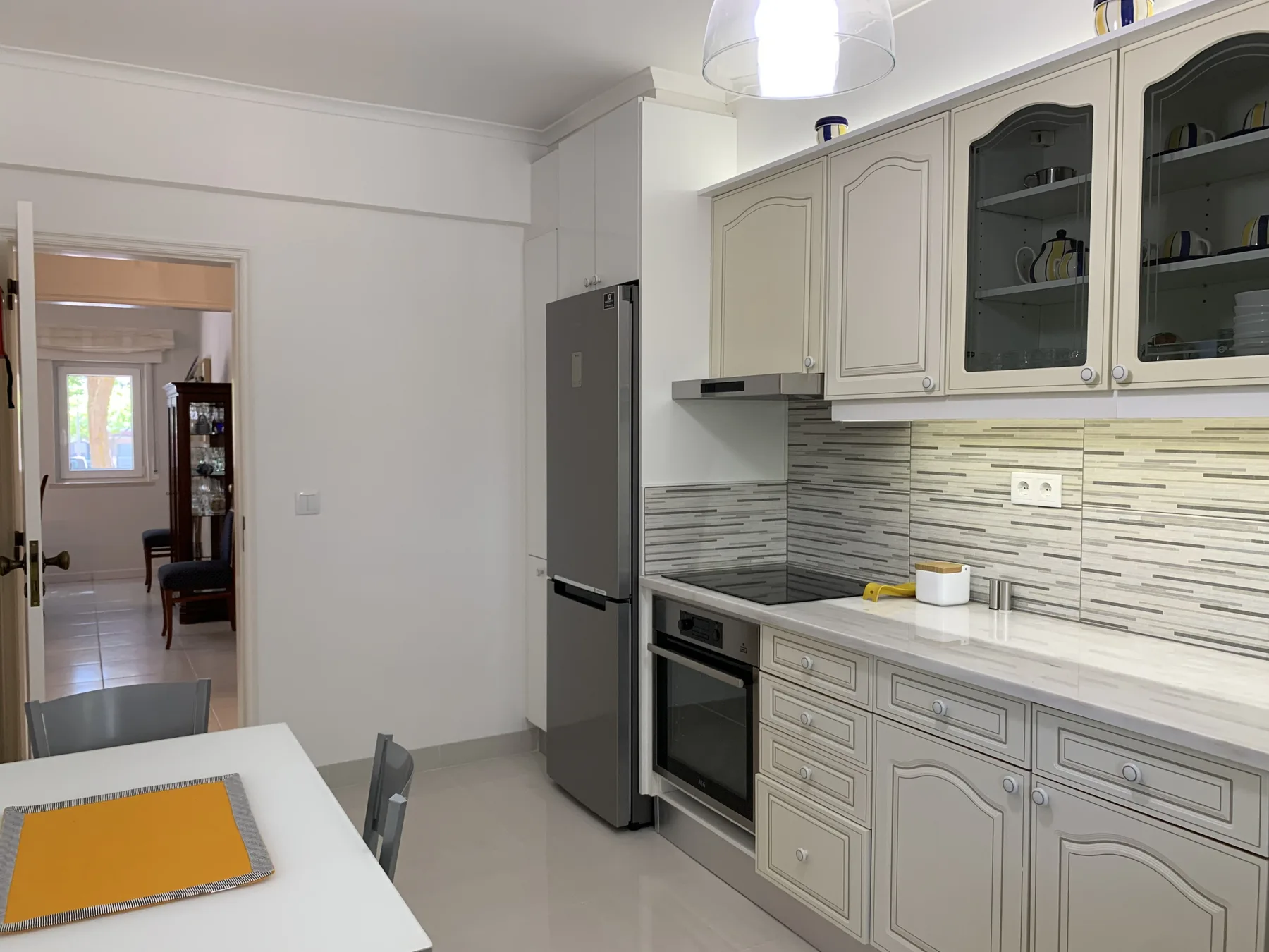 Cocina luminosa con armarios empotrados, refrigerador y mesa de comedor.
