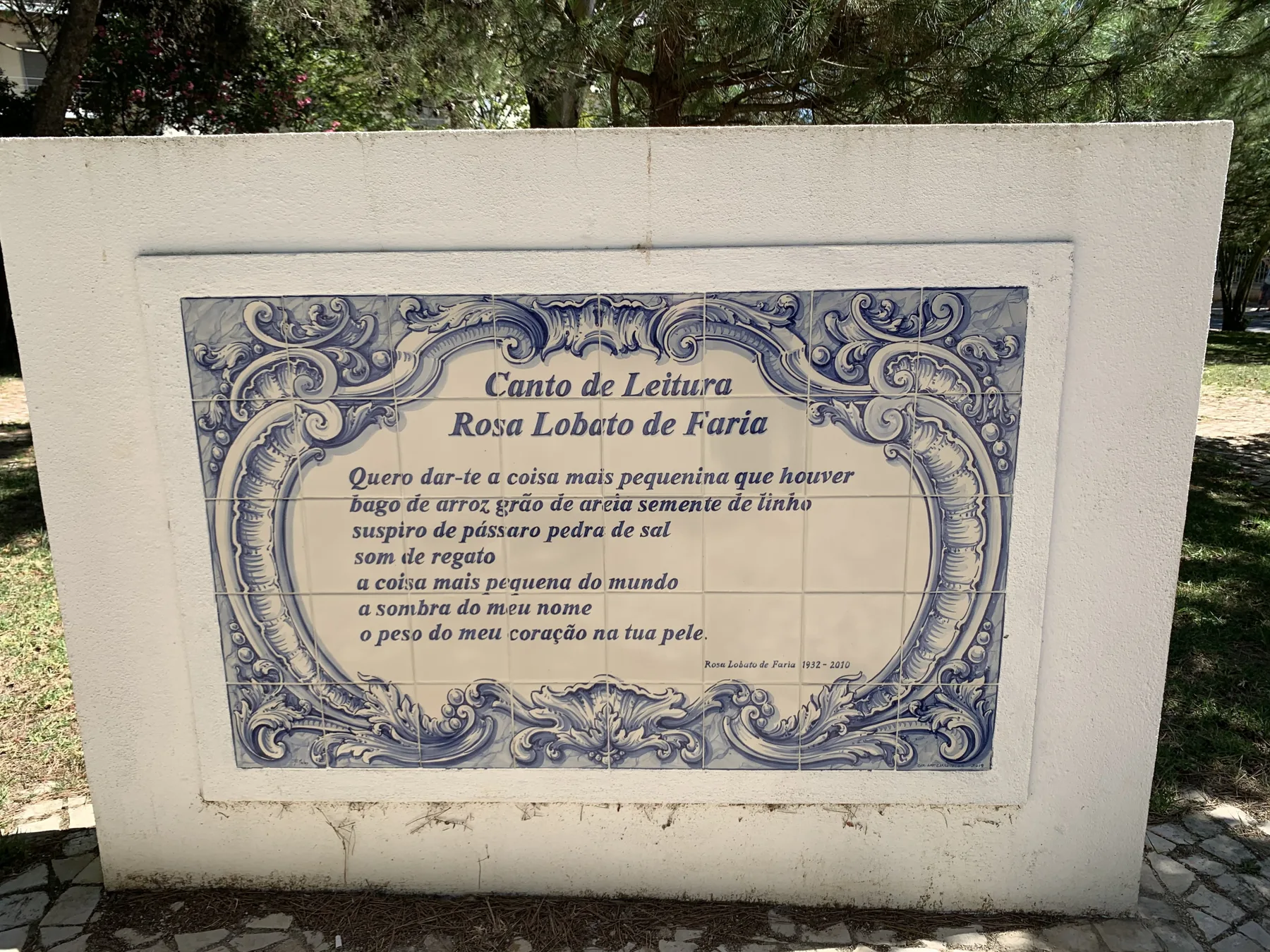 Una placa de cerámica decorada con poesía está montada en un muro blanco al aire libre.