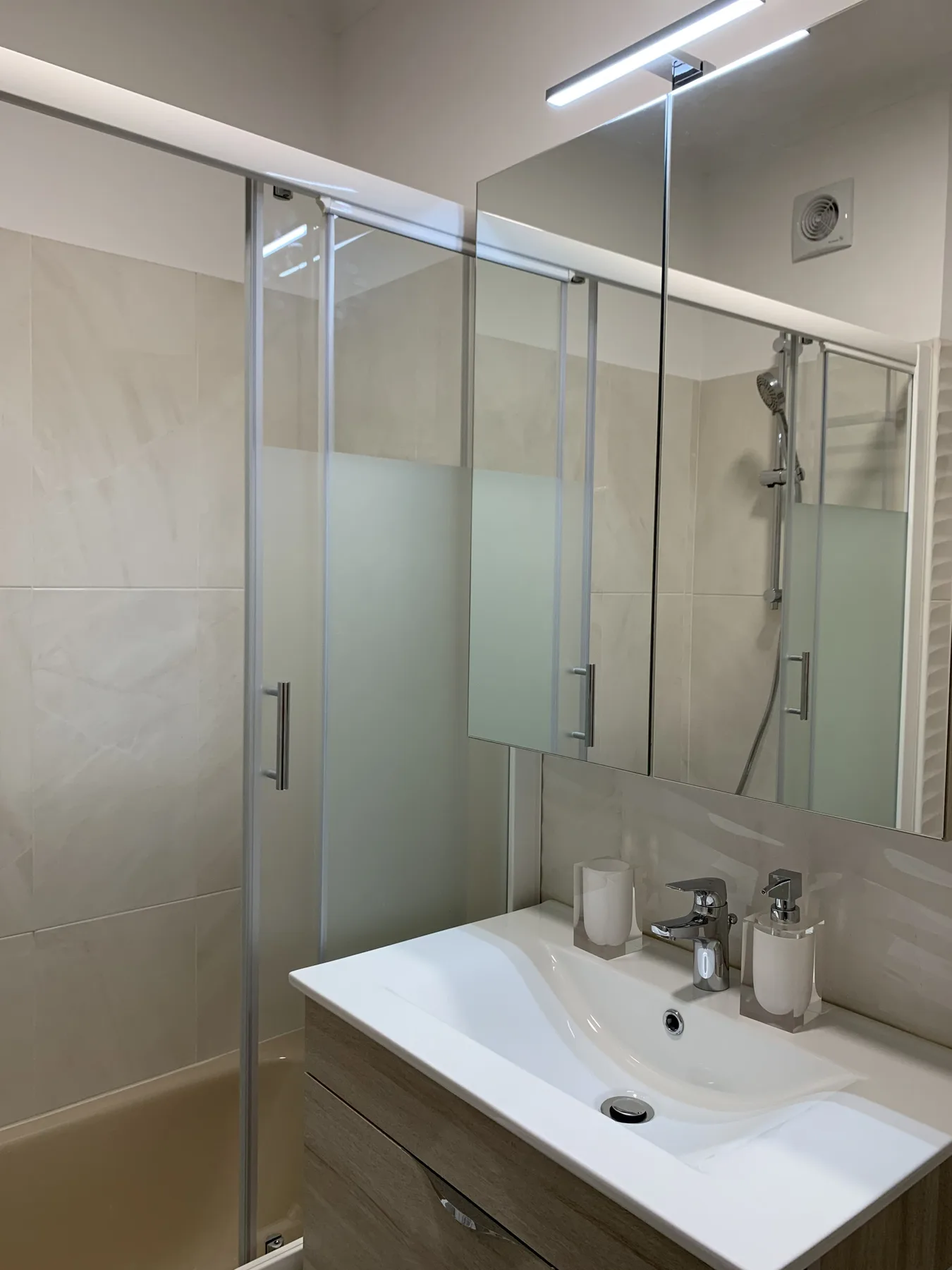 Un baño alicatado con ducha de vidrio y lavabo blanco.