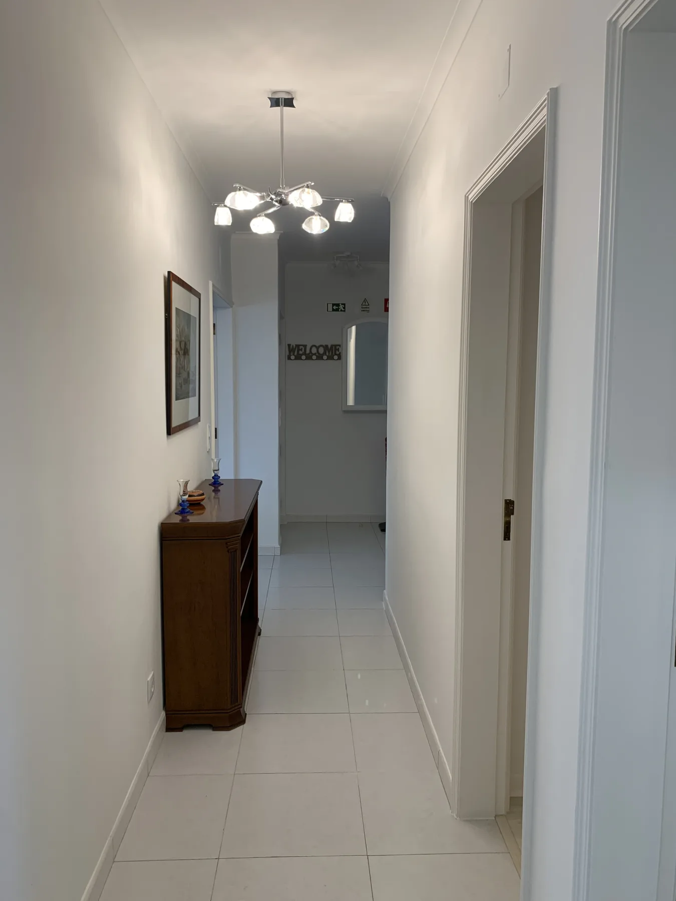 Un pasillo interior estrecho con paredes blancas, suelo de baldosas y una consola de madera.