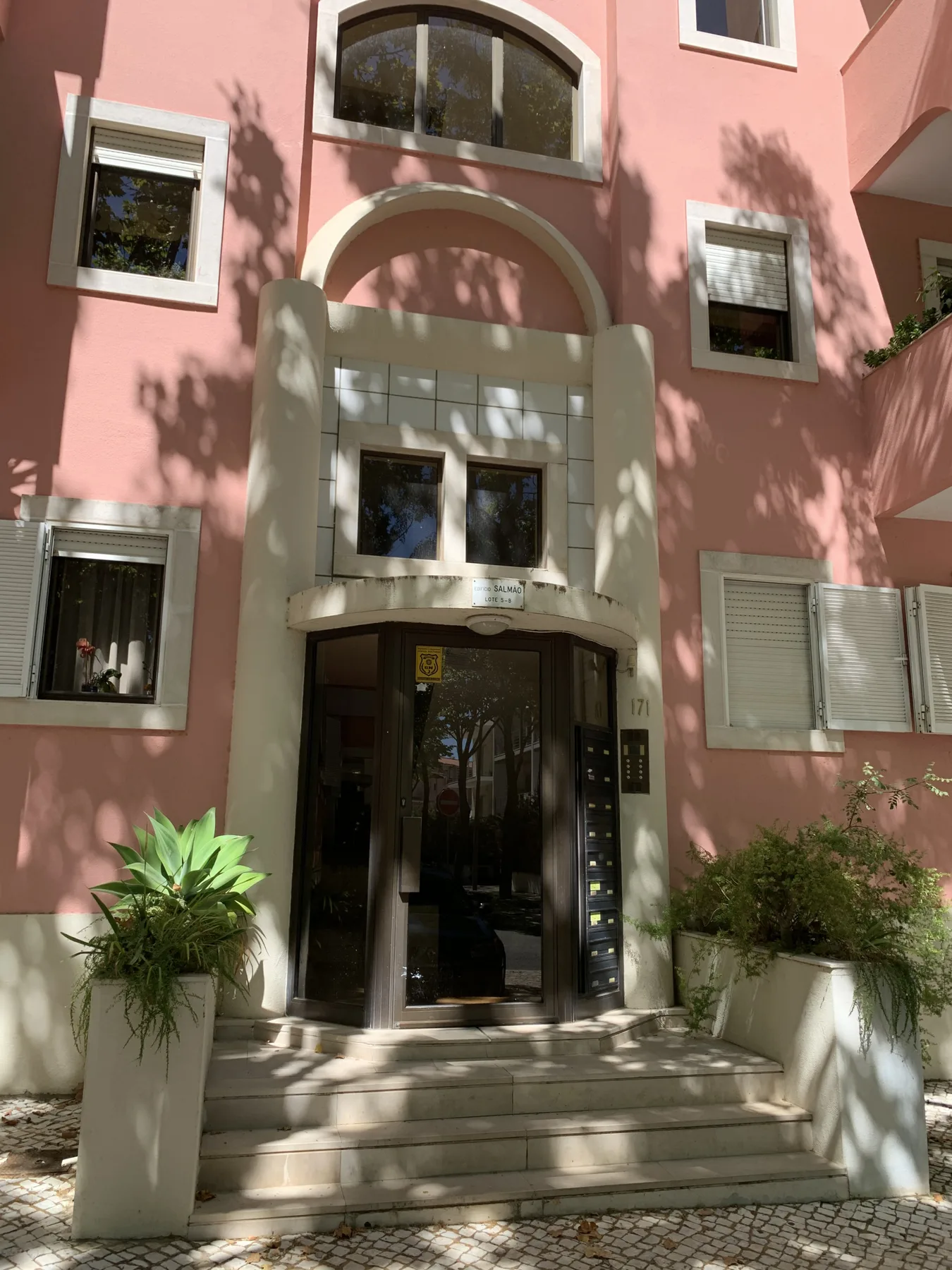 Entrada de un edificio rosa con puertas de cristal y escalones.