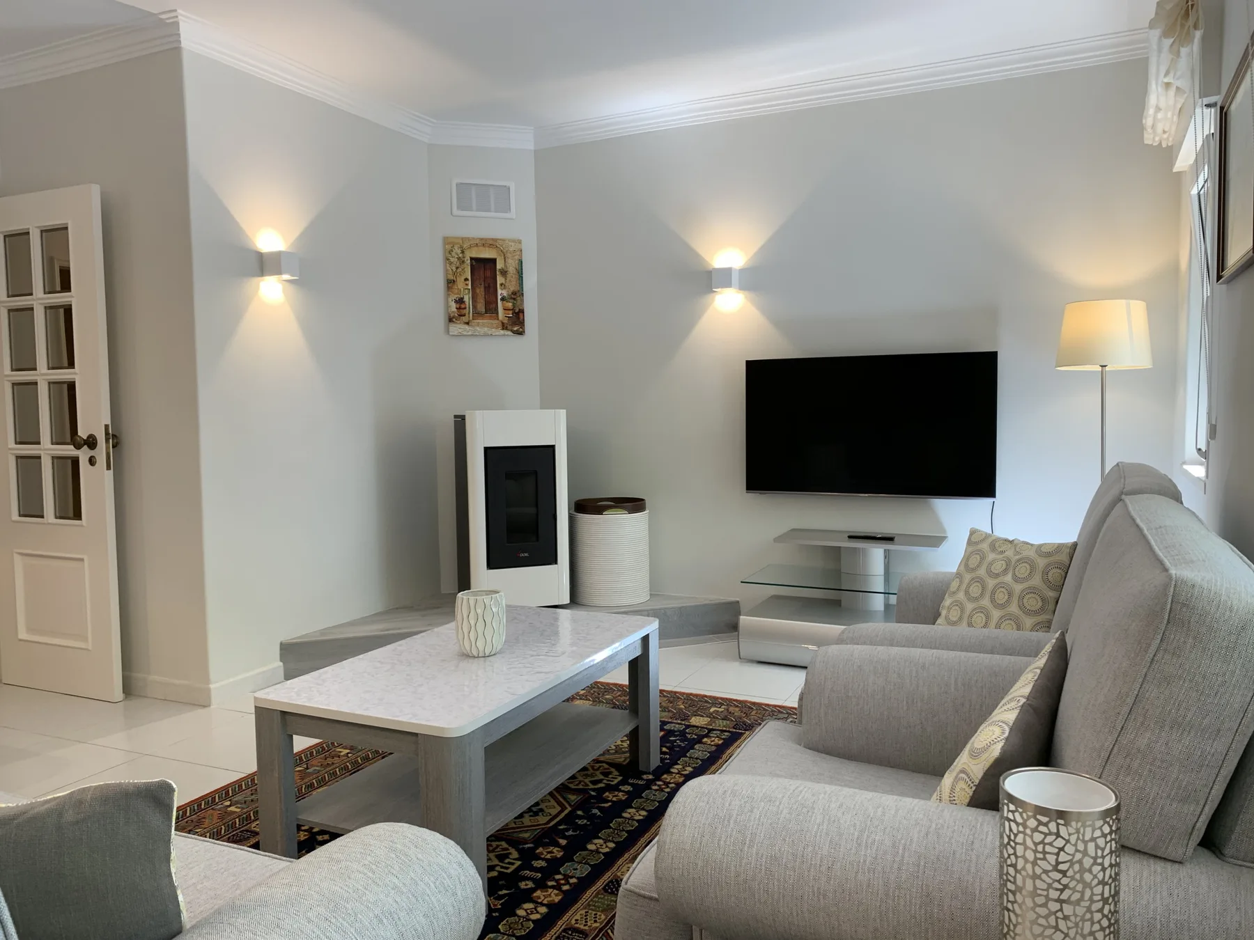 Una sala luminosa con asientos grises, una mesa de centro y un televisor en la pared.